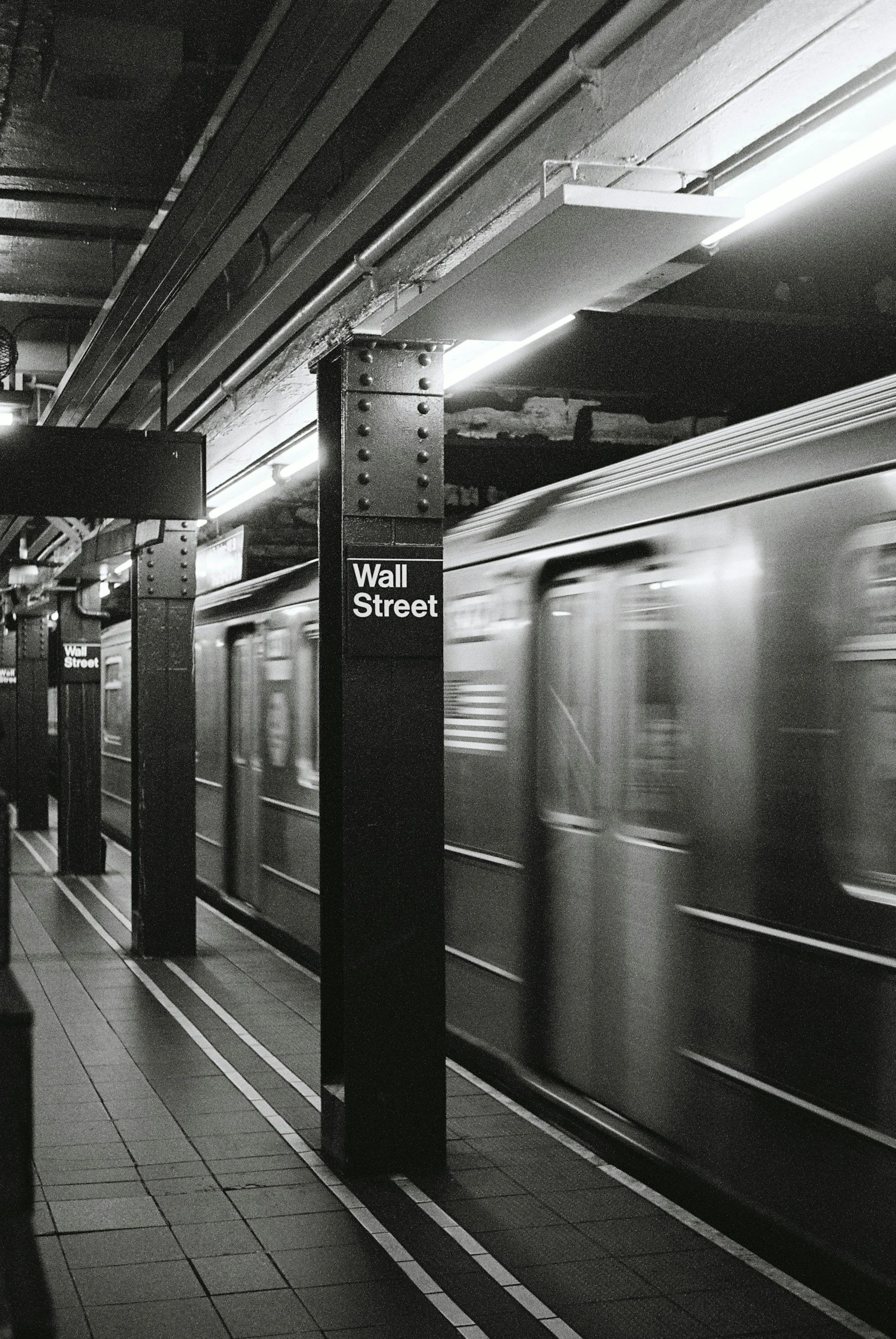 A black and white photo of the Wall Street subway station with a moving train in New York City.