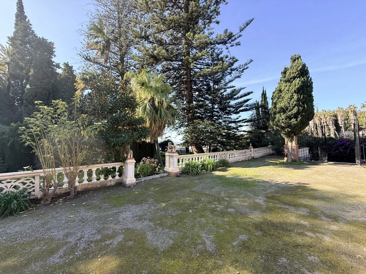 View of a garden with trees, a white decorative fence, and a grassy area on a sunny day.