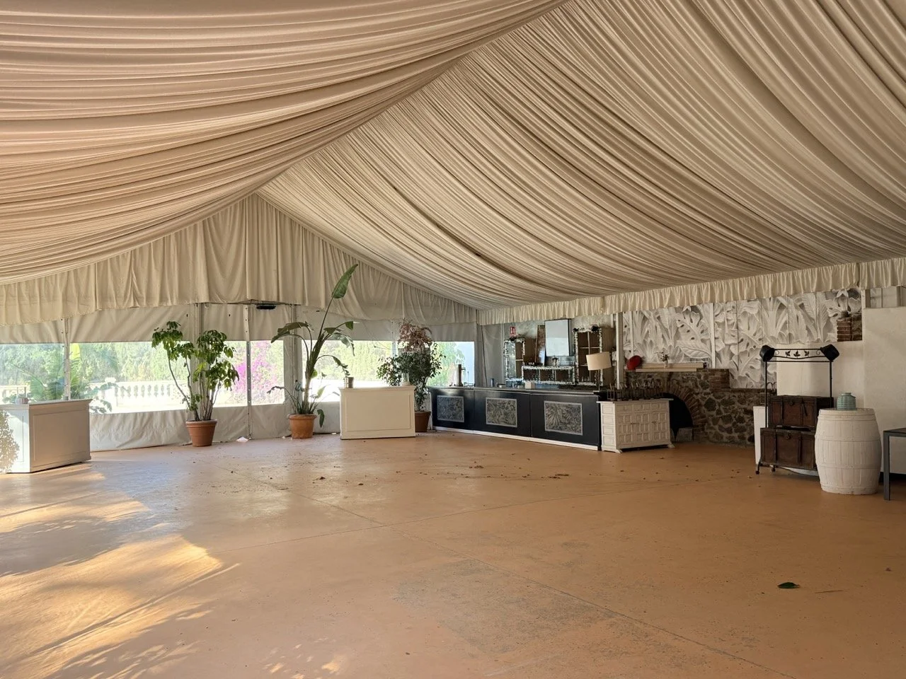 Empty event tent with draped ceiling, potted plants, a bar area, and decorative wall paneling.