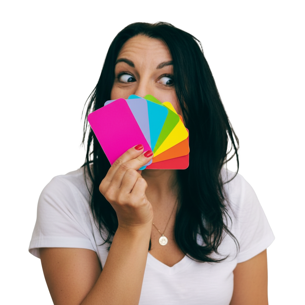 Woman with dark hair holding colorful color swatches covering her nose, with wide eyes looking to the side, wearing a white shirt.