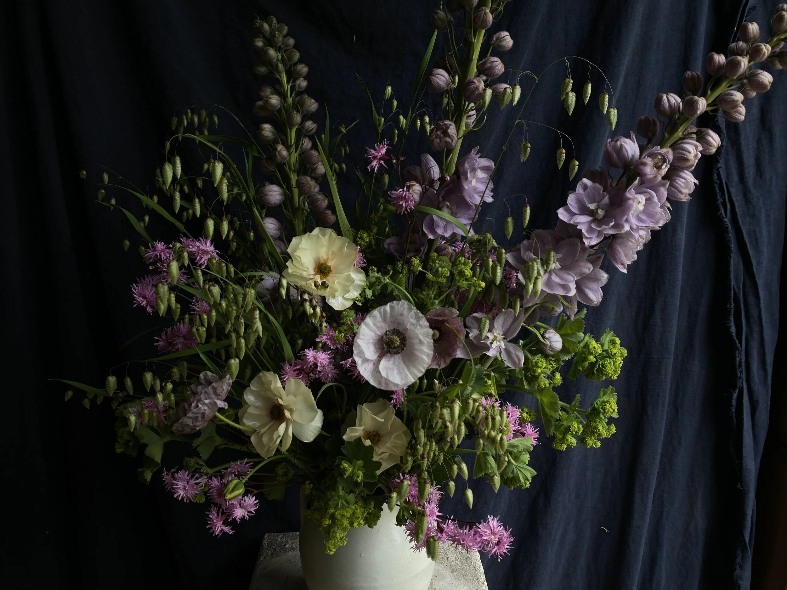 A flower arrangement in a white vase containing purple and green flowers with a dark background.