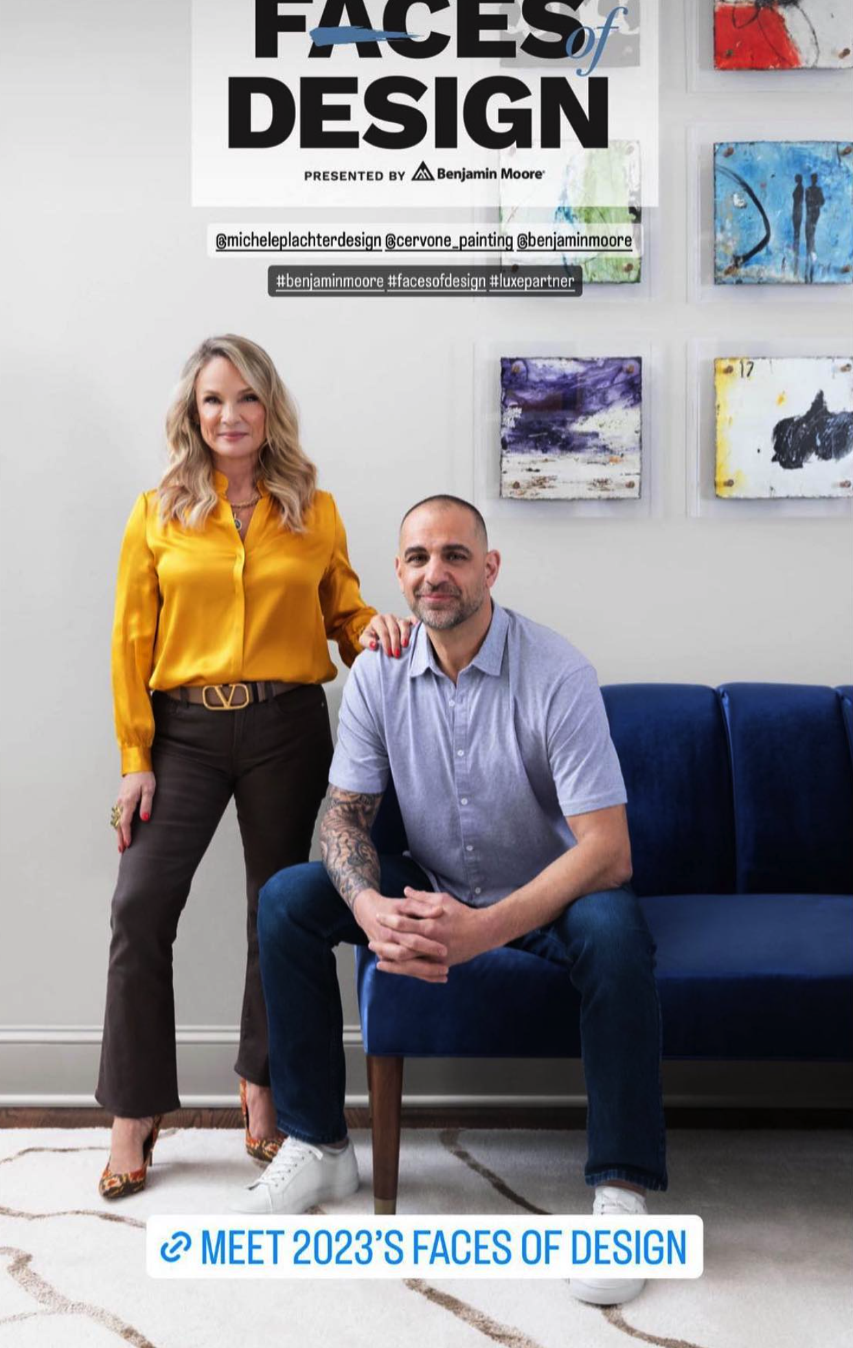 A photo of two people, a woman standing to the left wearing a yellow blouse and brown pants, and a man sitting on a blue couch wearing a light gray shirt and dark jeans, in an art gallery or office with abstract paintings on the wall behind them. The