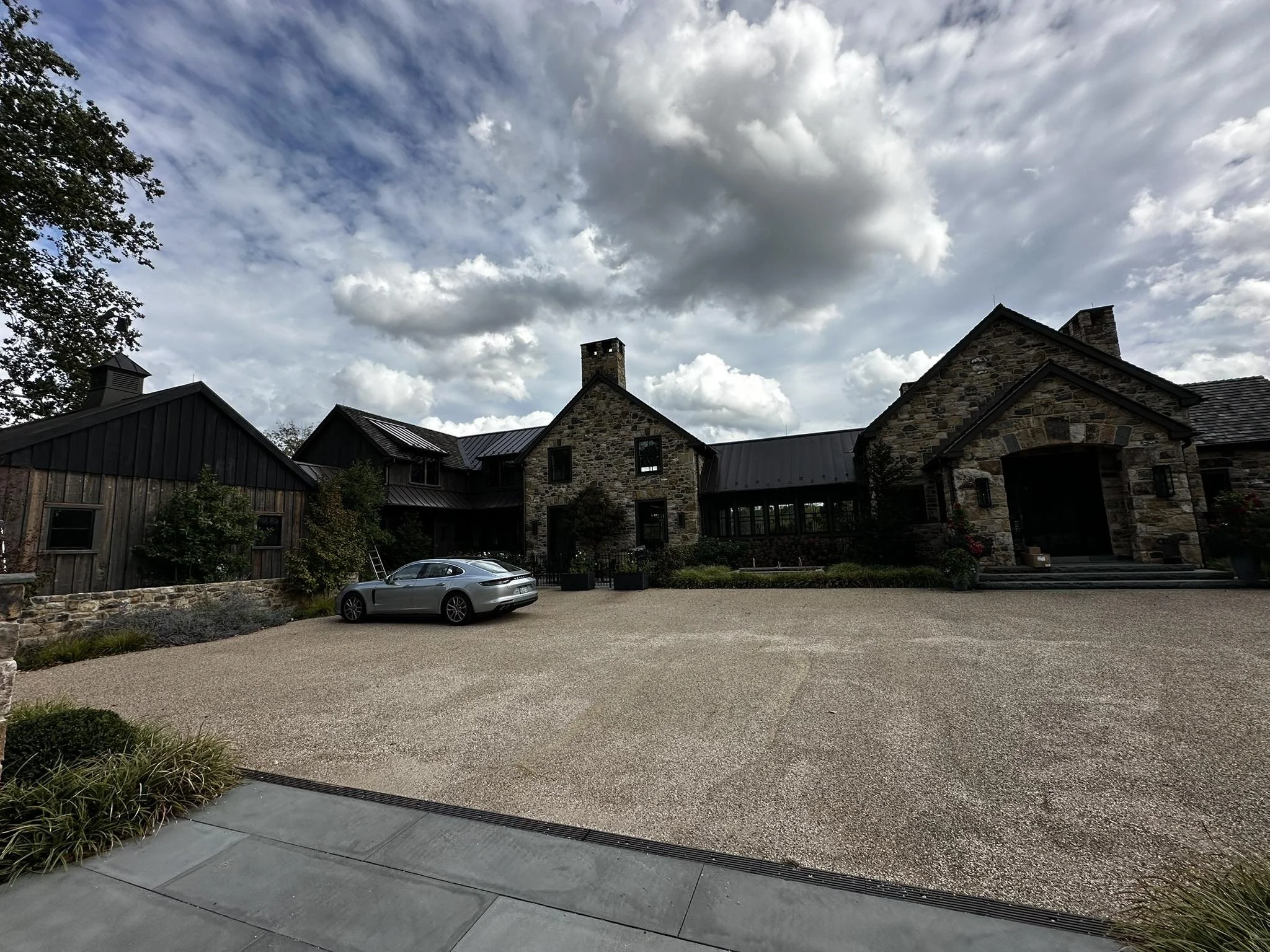 Cervone Painting Services Philadelphia Main Line - A large house with stone and wood exterior, a driveway with a silver car parked in front, and a cloudy sky above.
