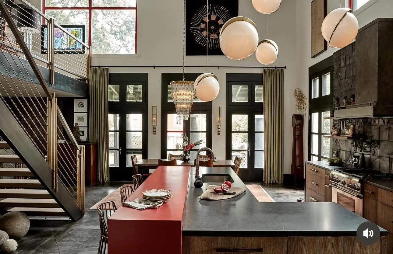 Cervone Painting Services Philadelphia Main Line - Modern kitchen with black and wooden cabinets, a red kitchen island, pendant lighting, a chandelier, large windows with curtains, and a staircase to the left.