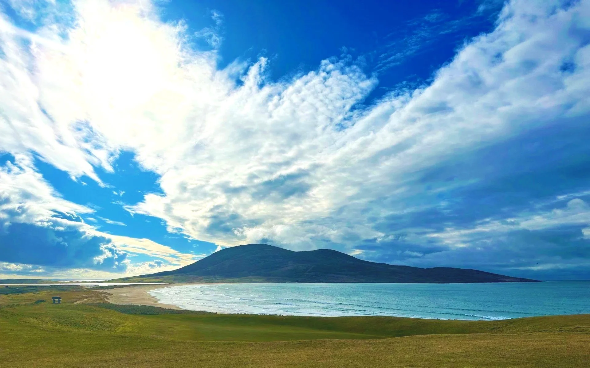 Scenic landscape with a mountain in the background, a body of water in the foreground, and a sky filled with clouds and sunlight.