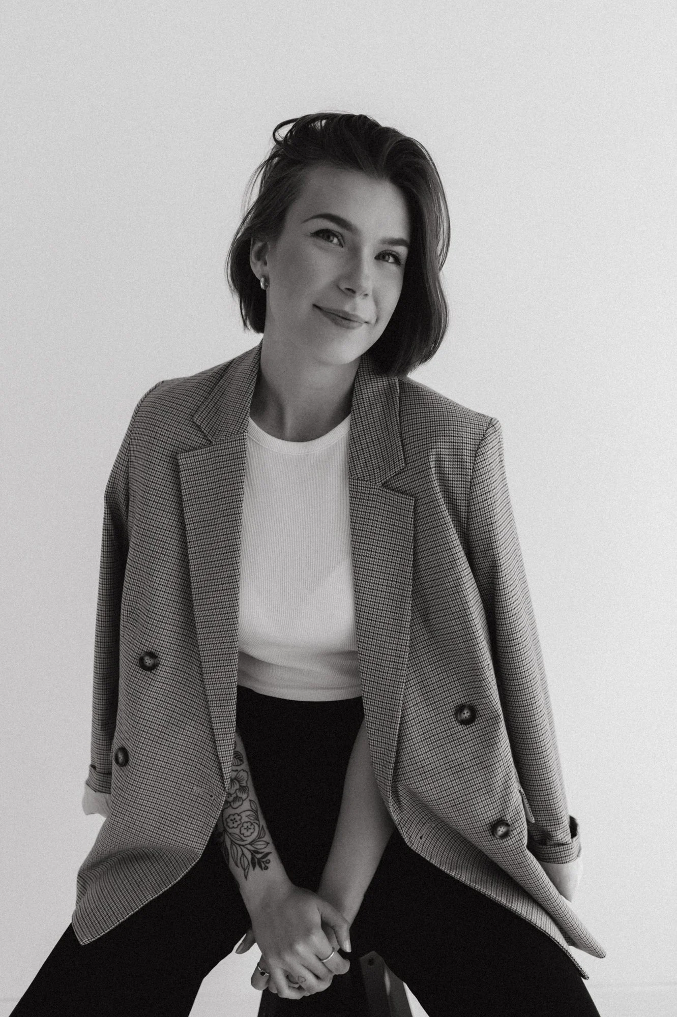 Mustavalkoinen kuva nuoresta naisesta hymyilemässä, istuu tuolilla, pukeutuneena bleiseriin ja t-paitaan.