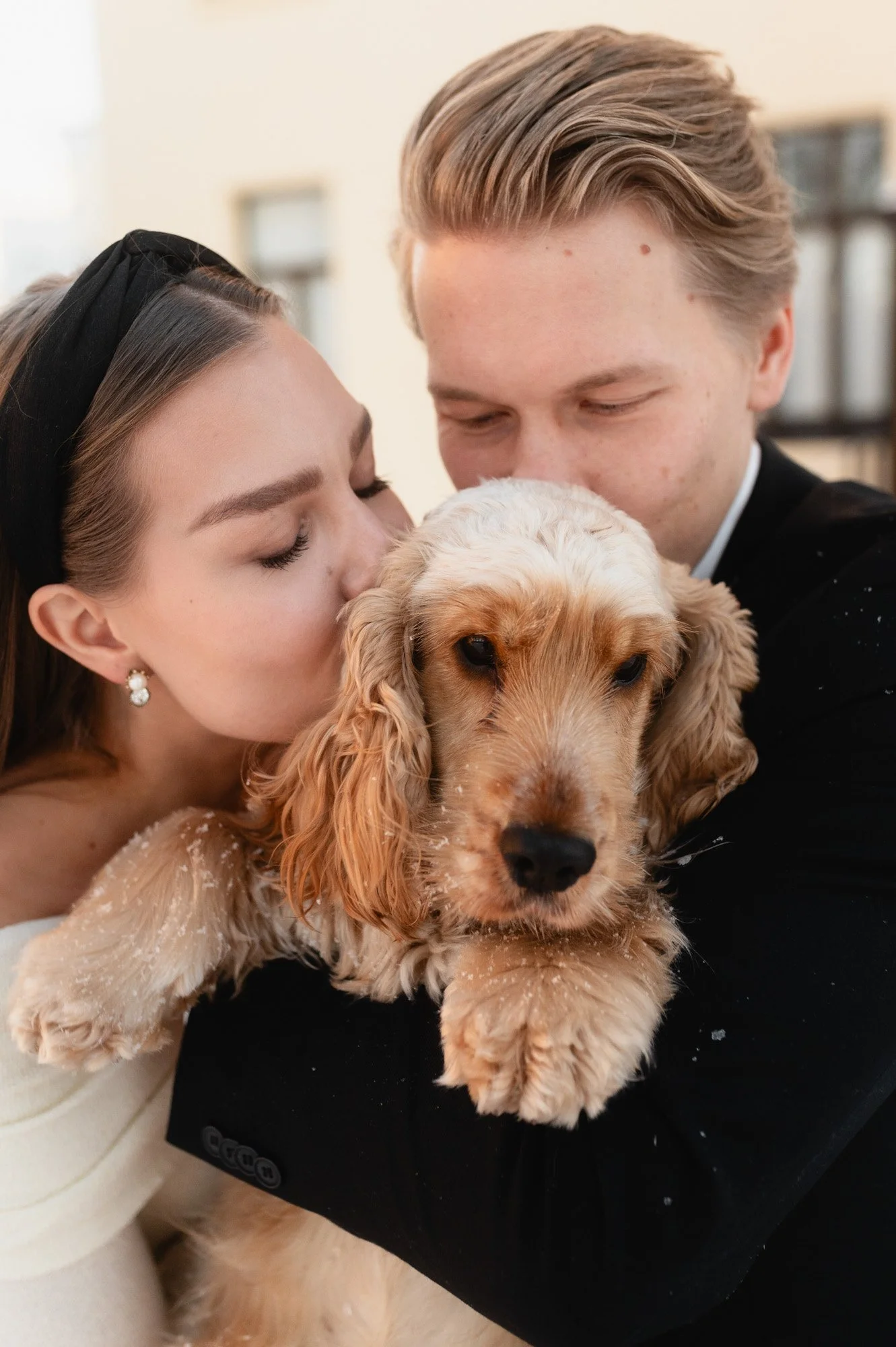 Kuva nuoresta parista halaamassa ja pussuttelemassa pientä koiraa, jolla on vaaleanruskea ja kermanvärinen turkki.