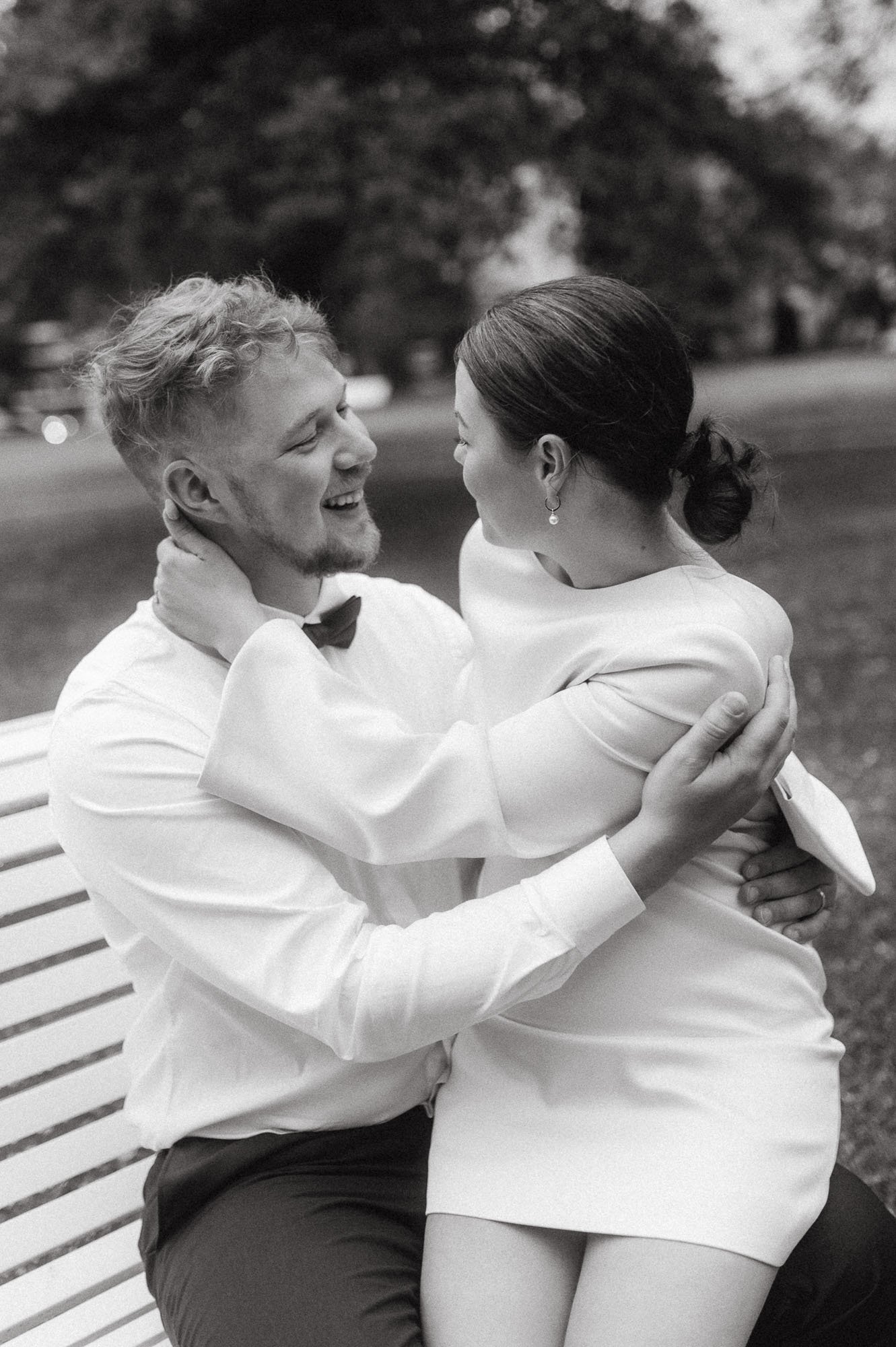 Mustavalkokuva onnellisesta pariskunnasta istuimella puistossa, hymyilevät ja halaavat toisiaan.