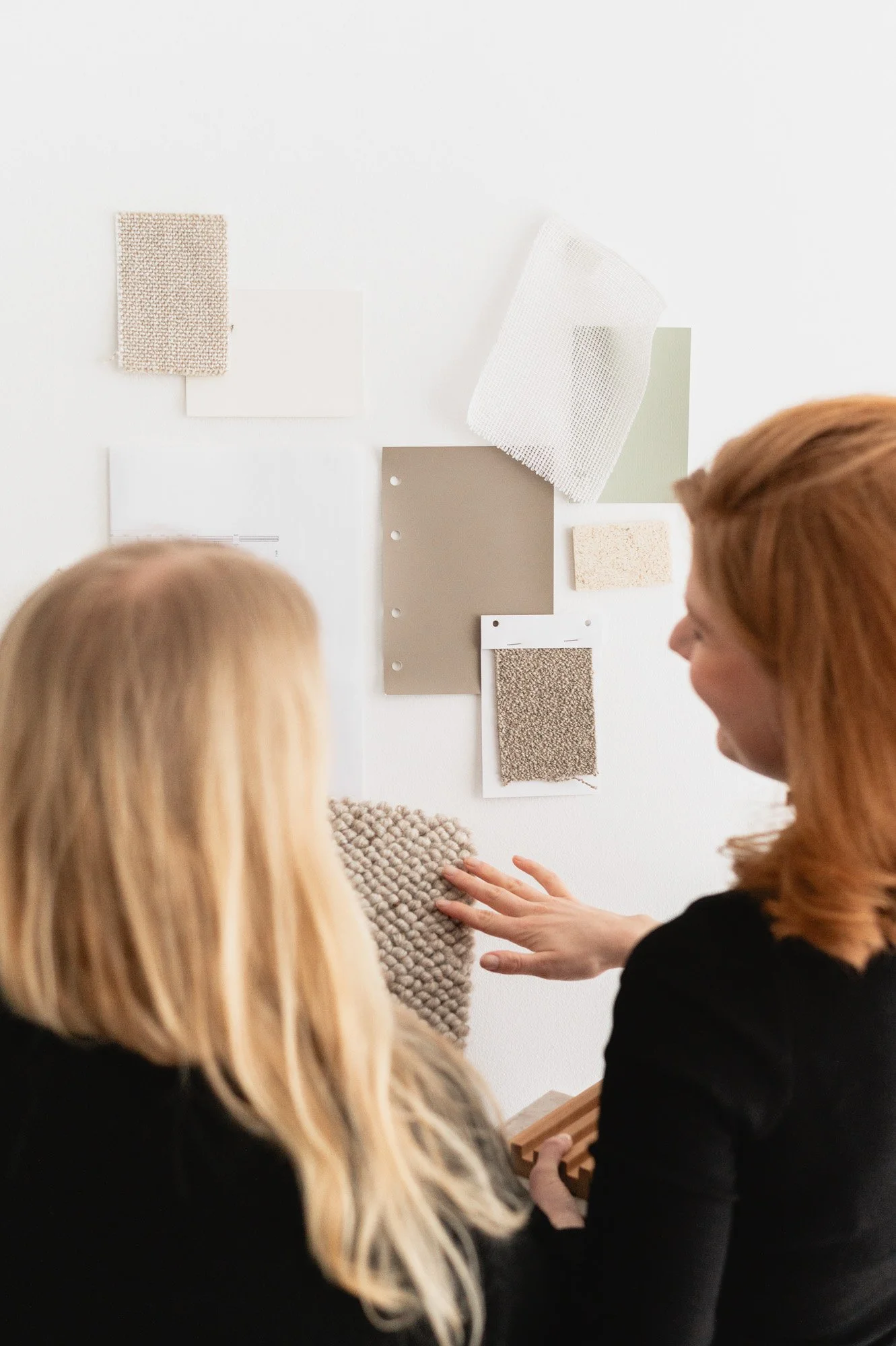Kaksi naista keskustelee sisustussuunnittelusta, katse kiinnittyy seinällä oleviin materiaalinäytteisiin. Sisustussuunnnittelu, brändikuvaus