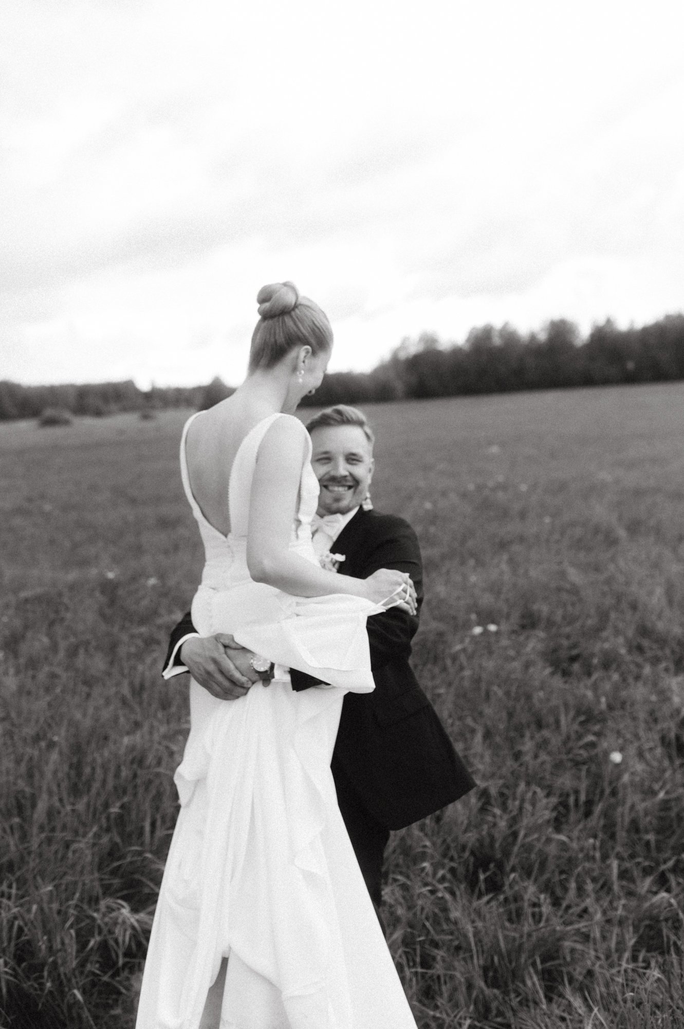 Mies ja nainen hääpuvuissa iloisesti halaamassa luonnonläheisessä maisemassa, mustavalkovalokuva.