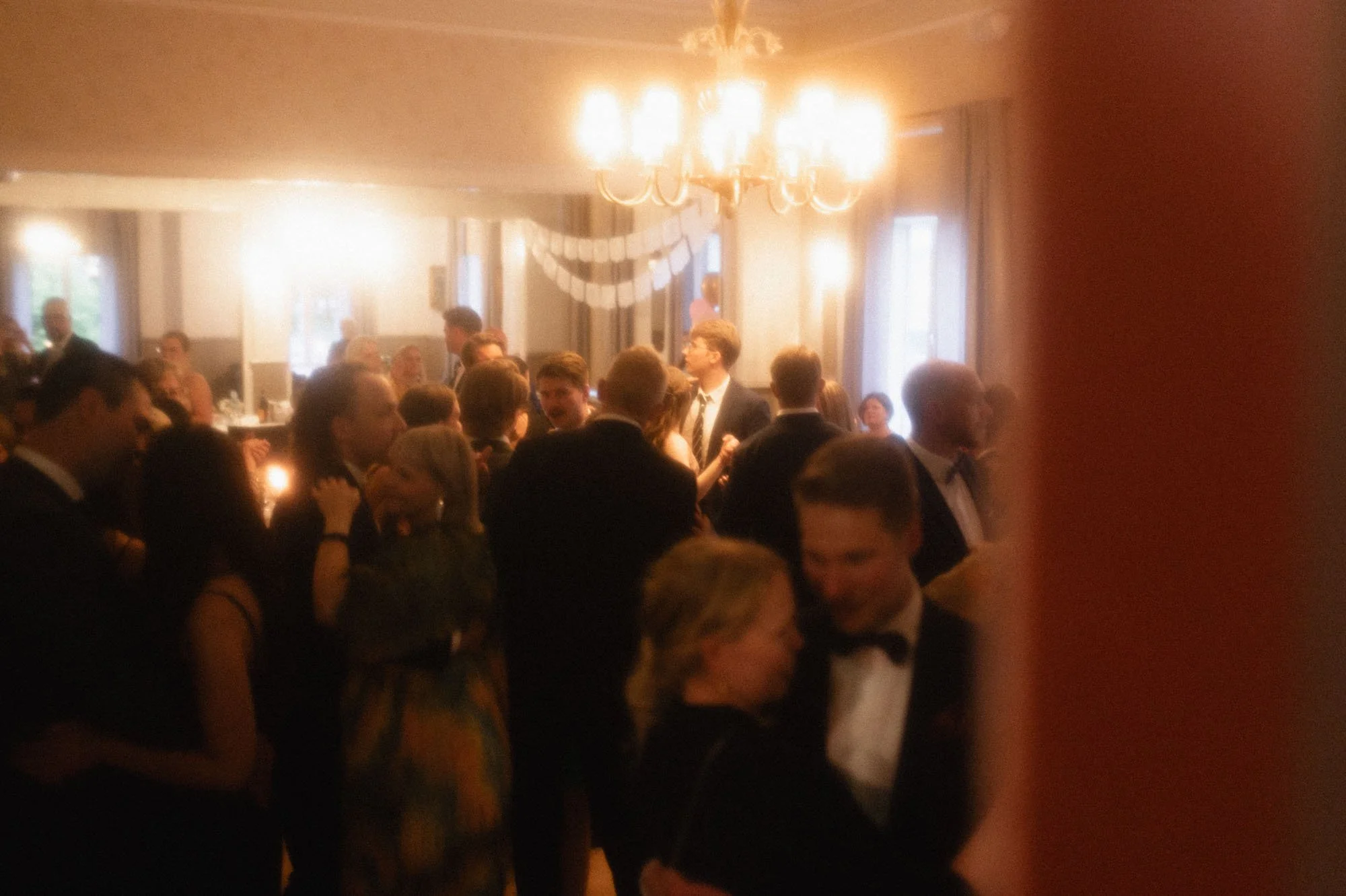 Häikäisevä hääjuhlan tanssilattia, jossa ihmiset pukuloistossa tanssivat ja juttelevat livemusiikin soidessa.