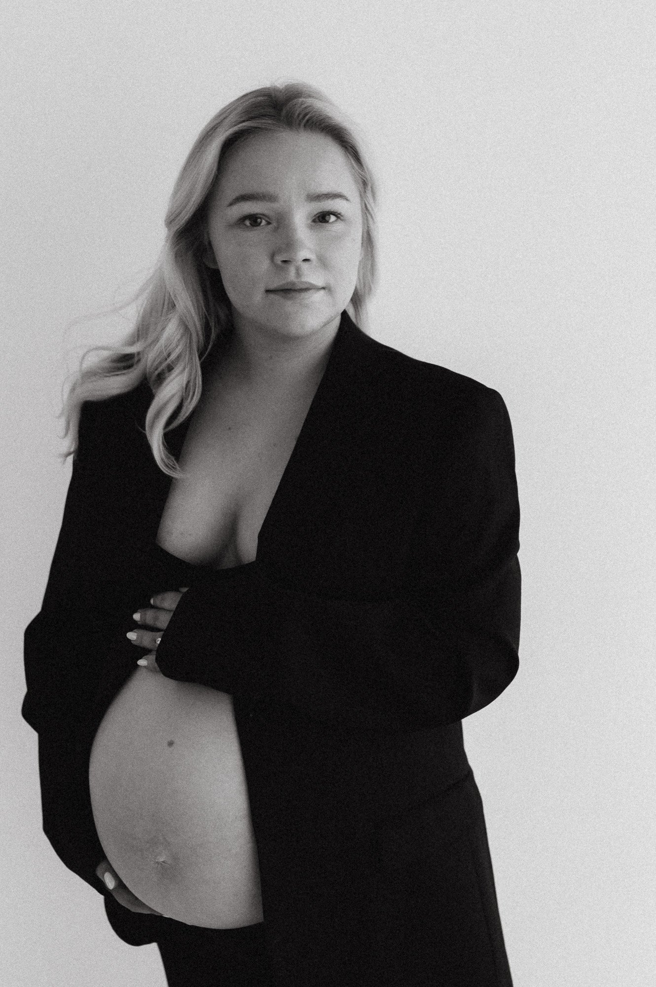 Mustavalkokuva naisesta, jolla on pitkä blondi hiukset, musta puku ja joka pitää kädessään paljastun vatsa. Hän katsoo kameraan vakavasti.