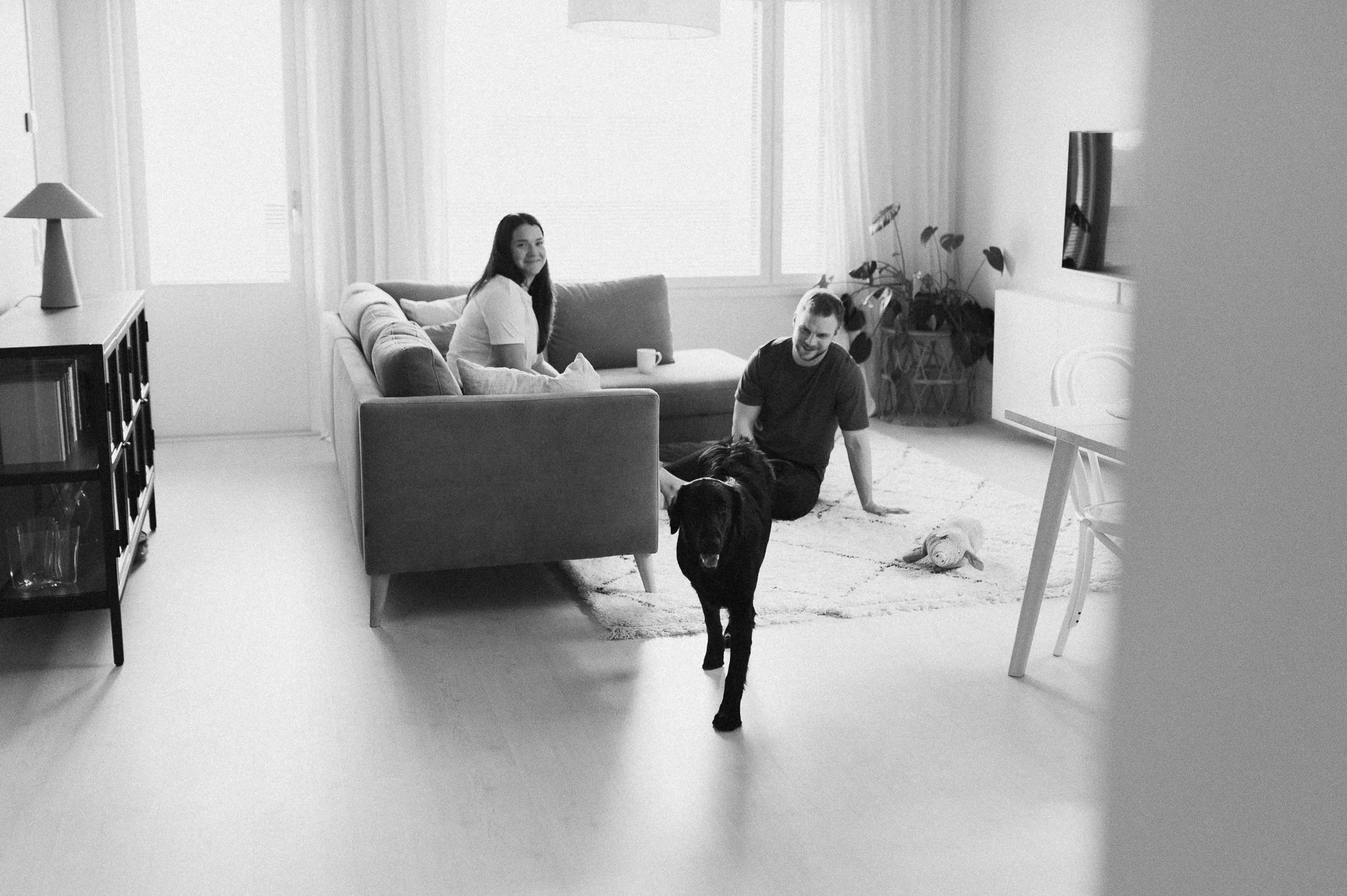 Kuvassa kolme ihmistä ja koira olohuoneessa, jossa on suuri ikkuna, sohva ja televisio.