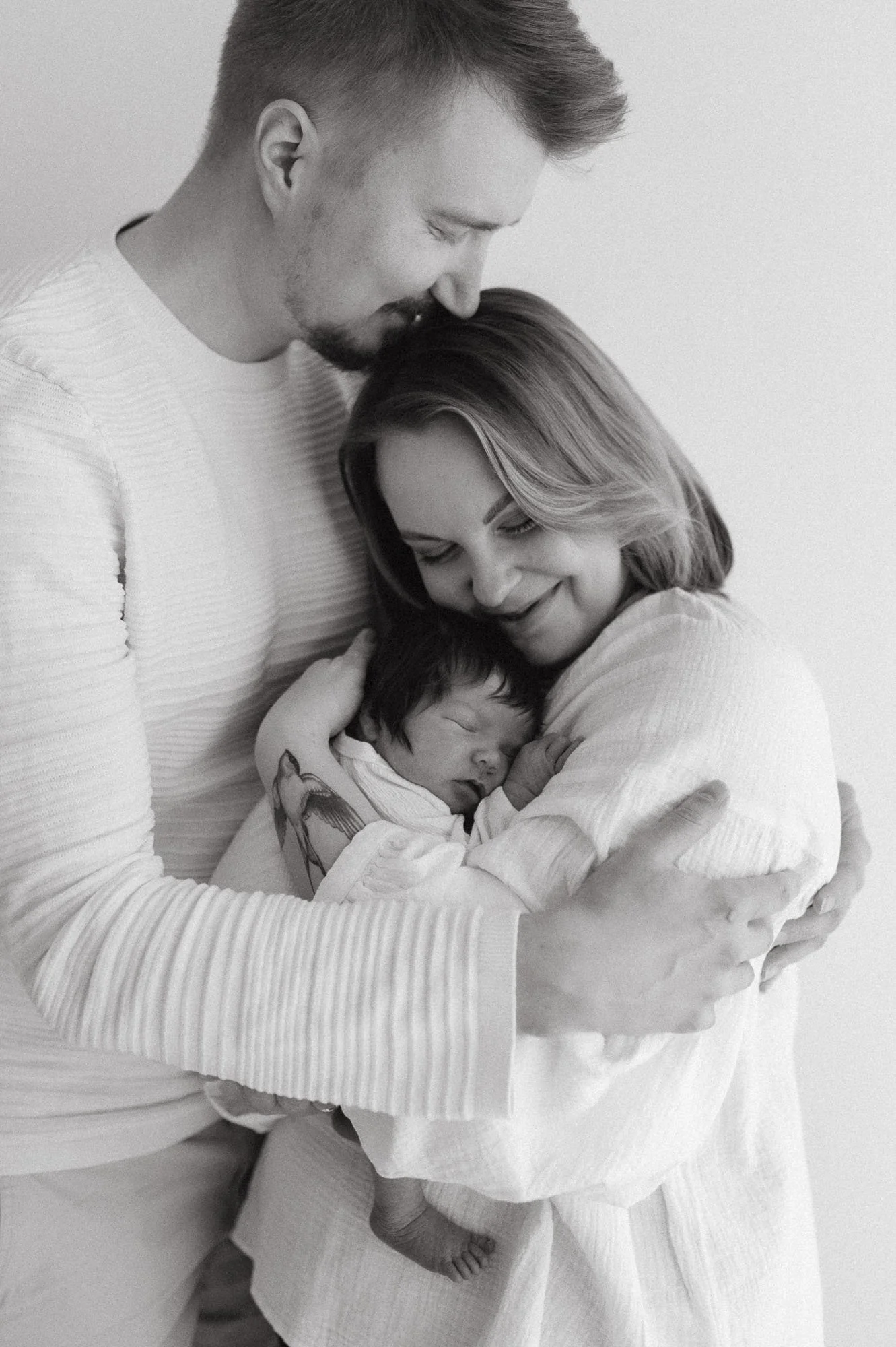 Vauva nukkuu sylissä, äiti ja isä halaavat ja katsovat hellästi heidän ympärillään.