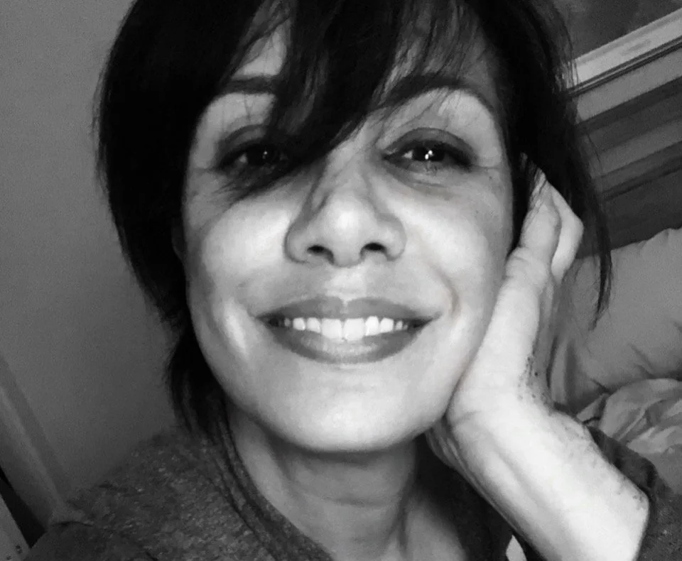 Black and white close-up photo of a smiling person with short, dark hair resting their face on their hand.