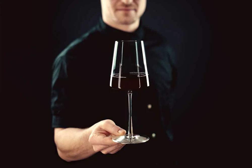 Person holding a clear wine glass with a dark background.