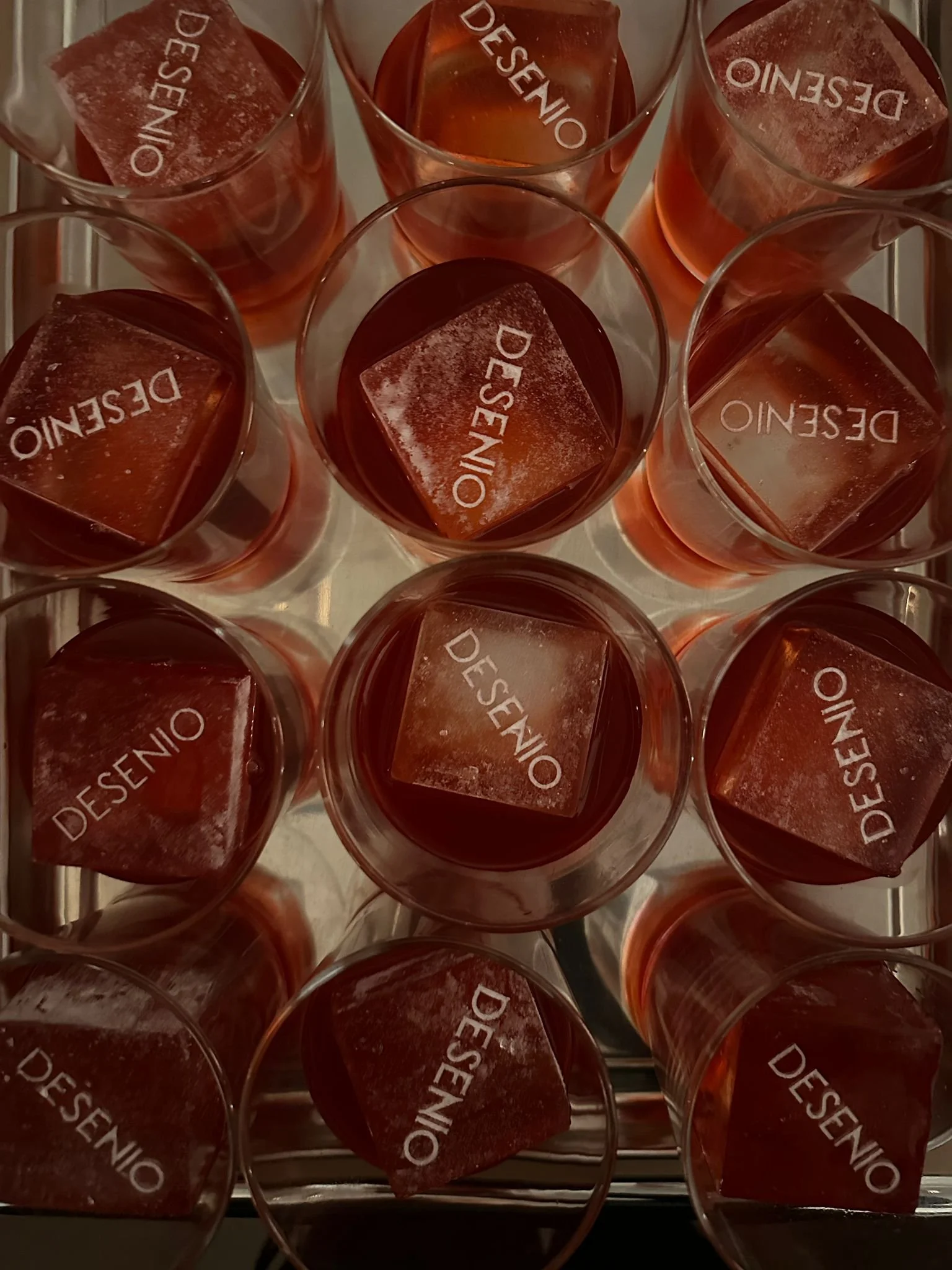 Several glasses of red dessert with ice cubes, each labeled 'DÉSÉNO', viewed from above.