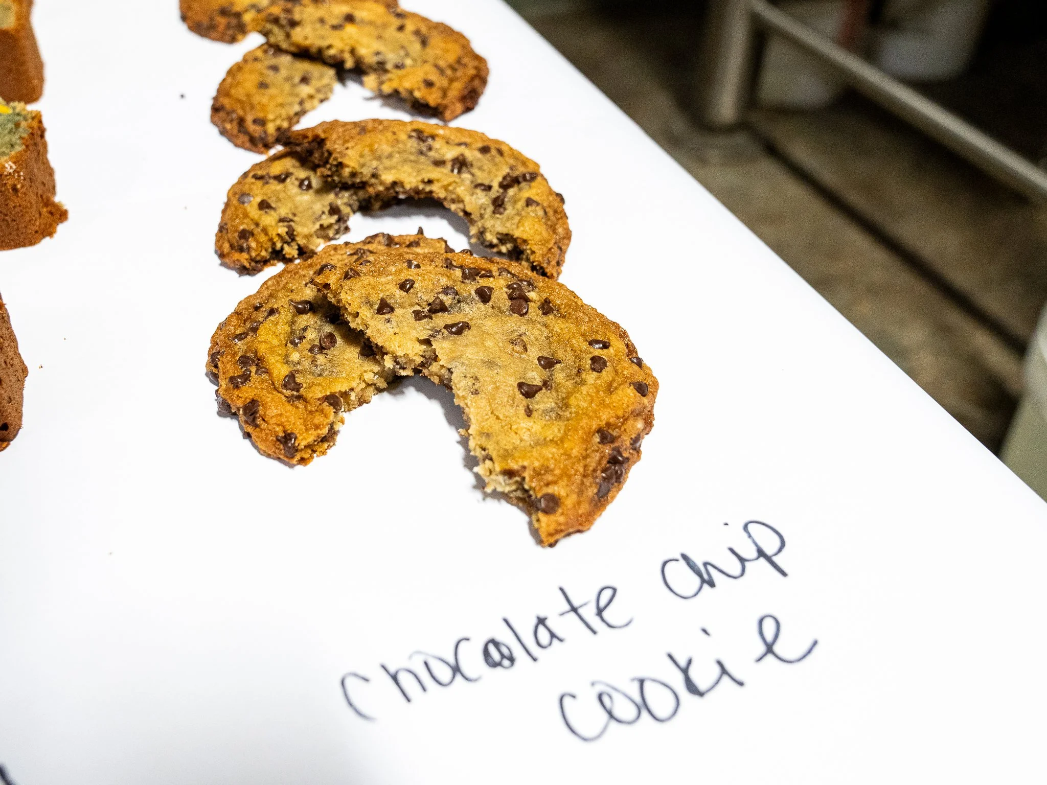 Chocolate chip cookie cut in half on white paper labeled 'chocolate chip cookie' with other cookies in the background.