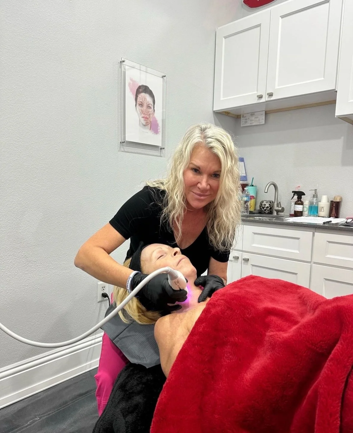 A woman is receiving a facial treatment from another person holding a device, in a spa or clinic setting.