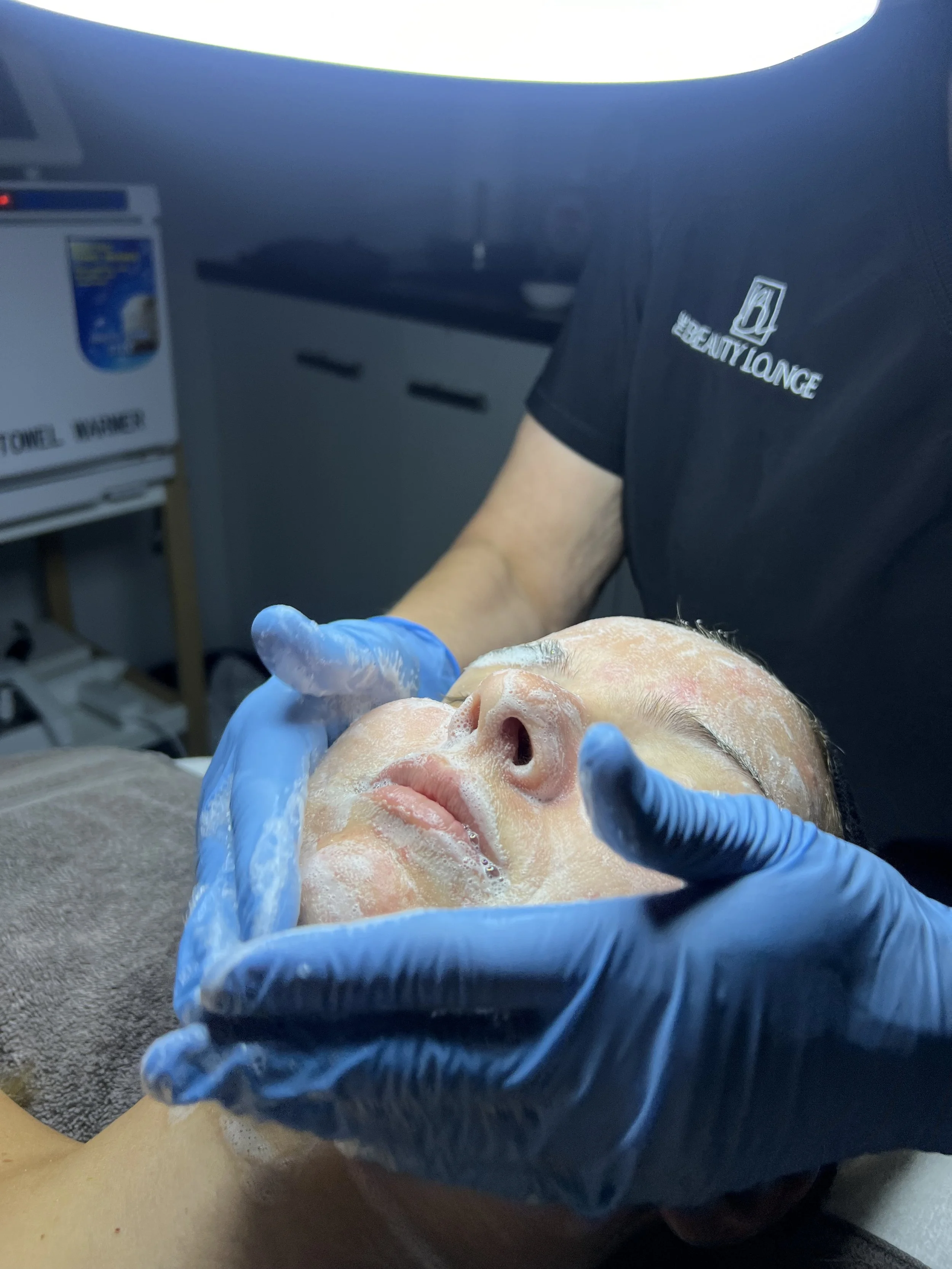 Person receiving a facial treatment with blue gloves in a spa.