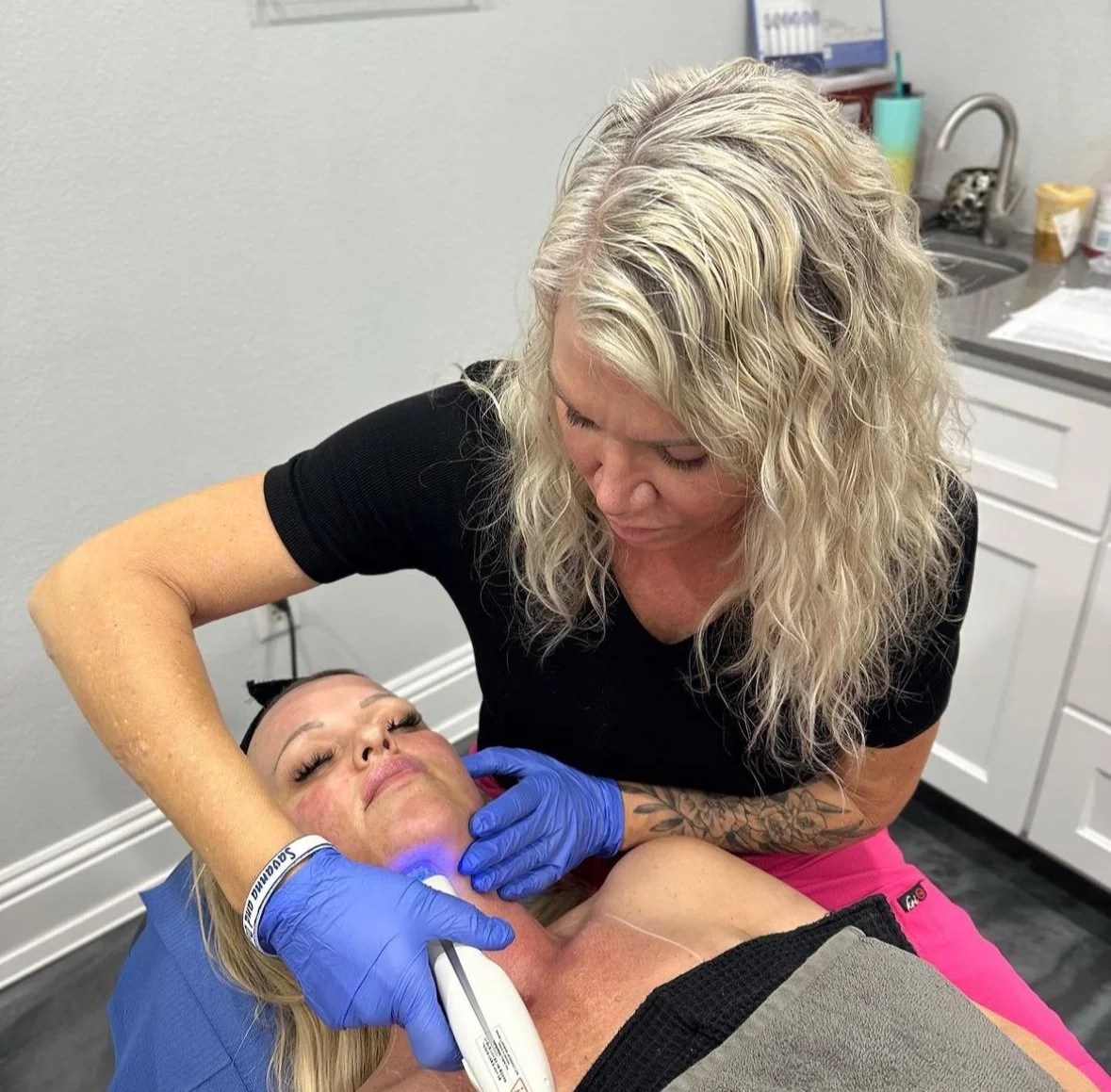 Esthetician performing a skin treatment on a woman using a handheld device, wearing blue gloves.