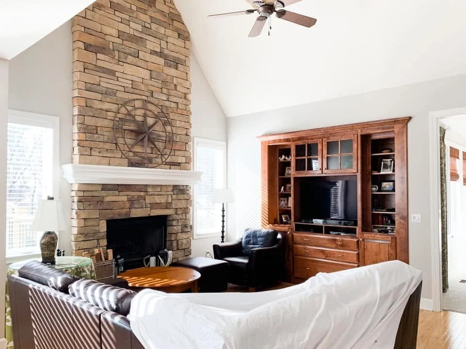 Finished Falcon Lakes living room with bright white vaulted ceiling, warm gray walls and stone fireplace.