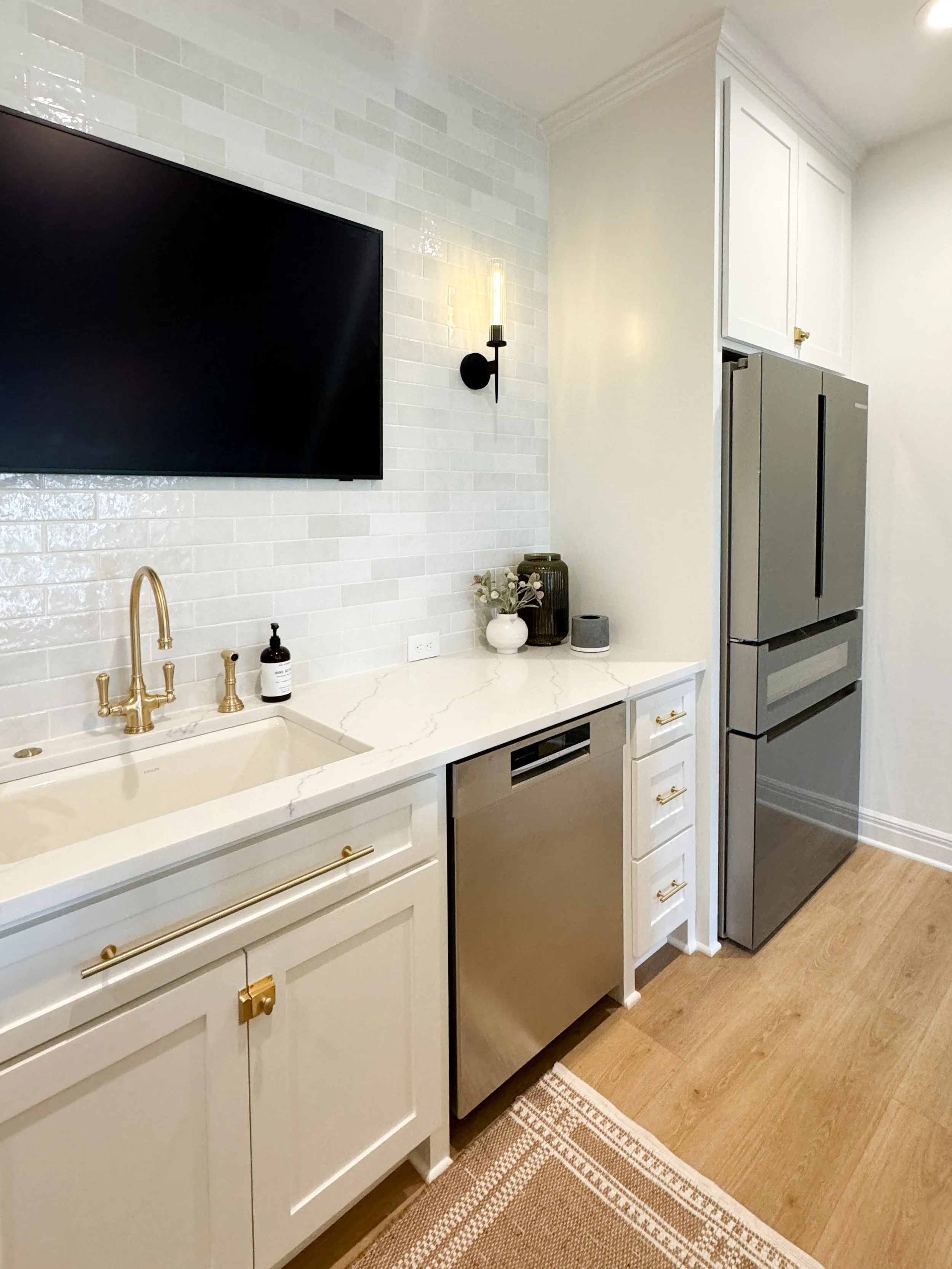 Finished white basement kitchenette with brass faucet, tile backsplash and refrigerator.