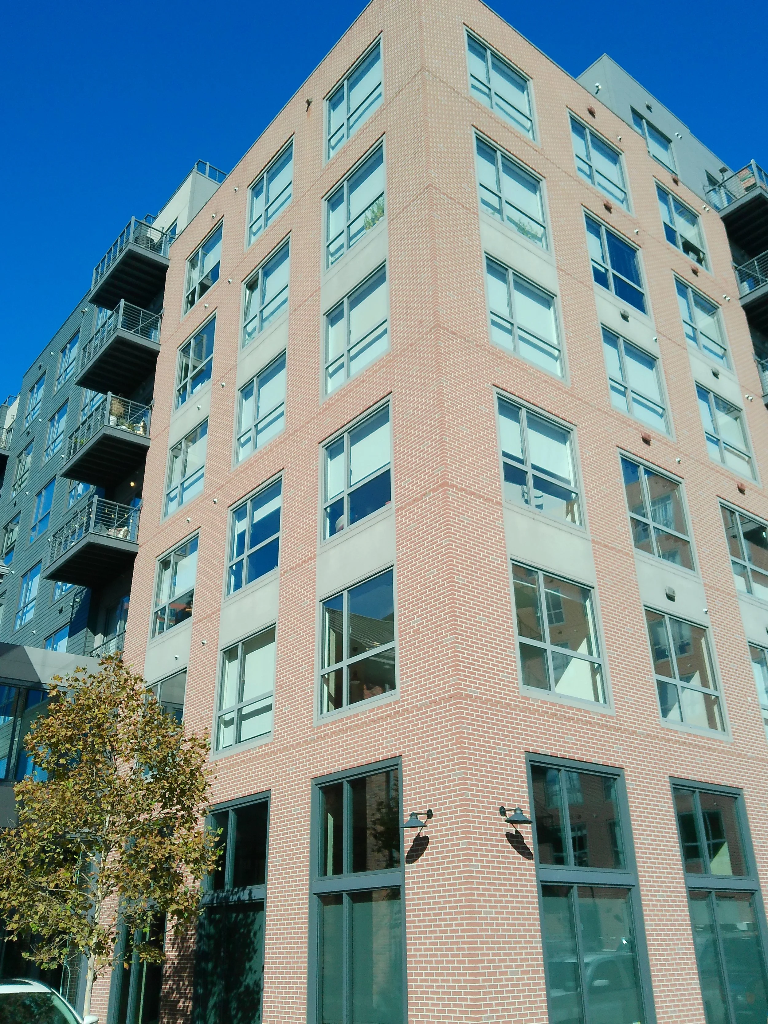 A tall modern brick apartment building with large windows and balcony details, set against a clear blue sky.