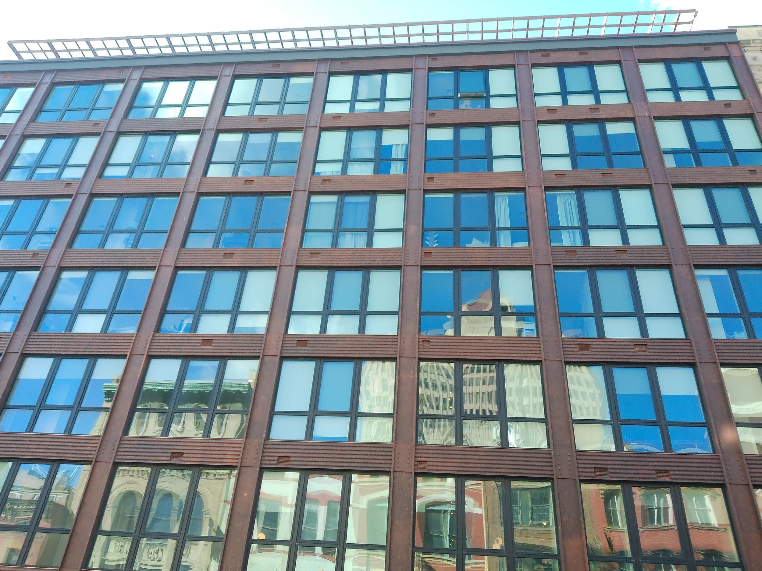 Reflections of surrounding buildings on the glass windows of a modern multi-story office building.