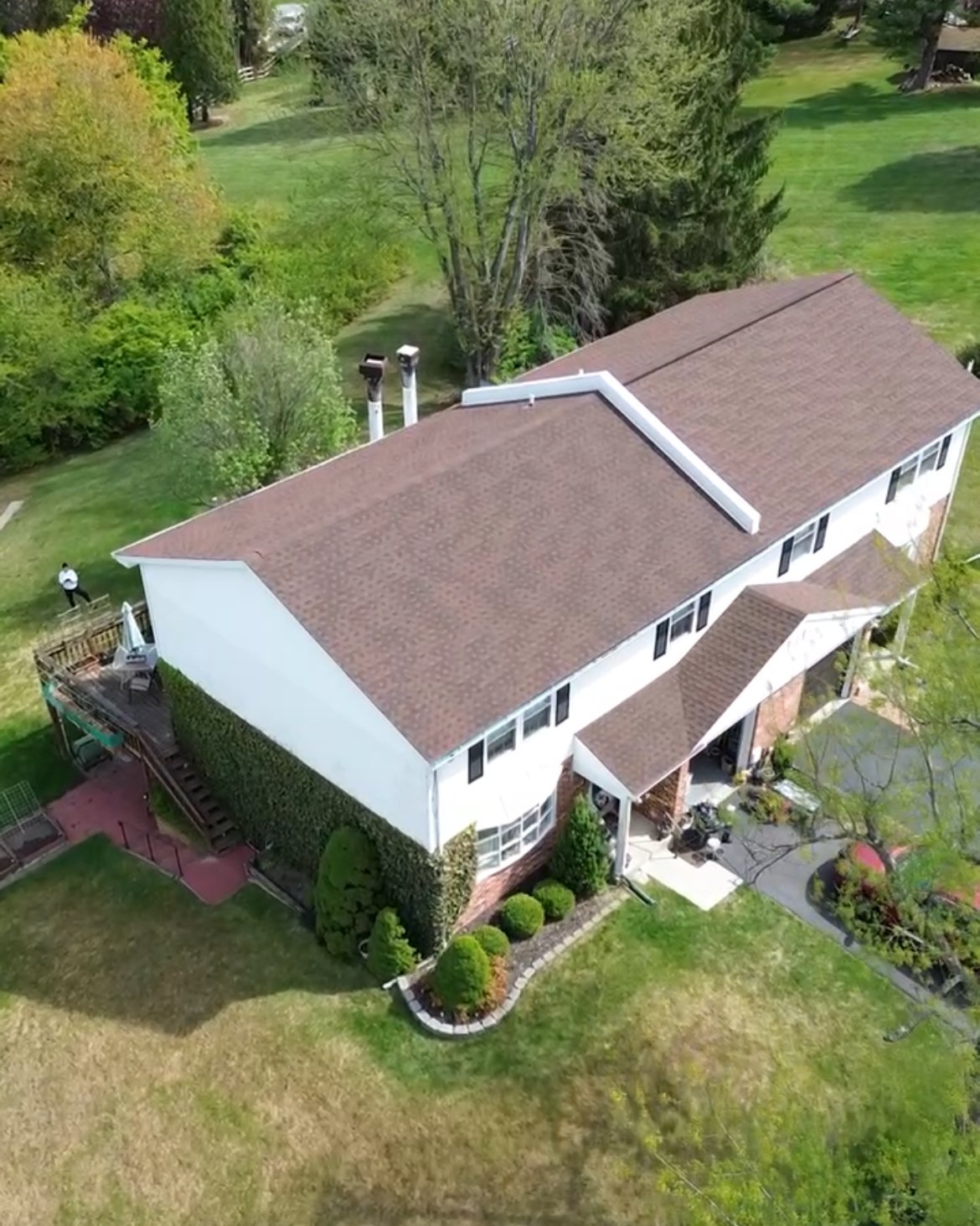 Aerial view of a two-story house with a brown roof, white walls, and a small front porch, surrounded by a well-maintained lawn and trees in Exton, PA.