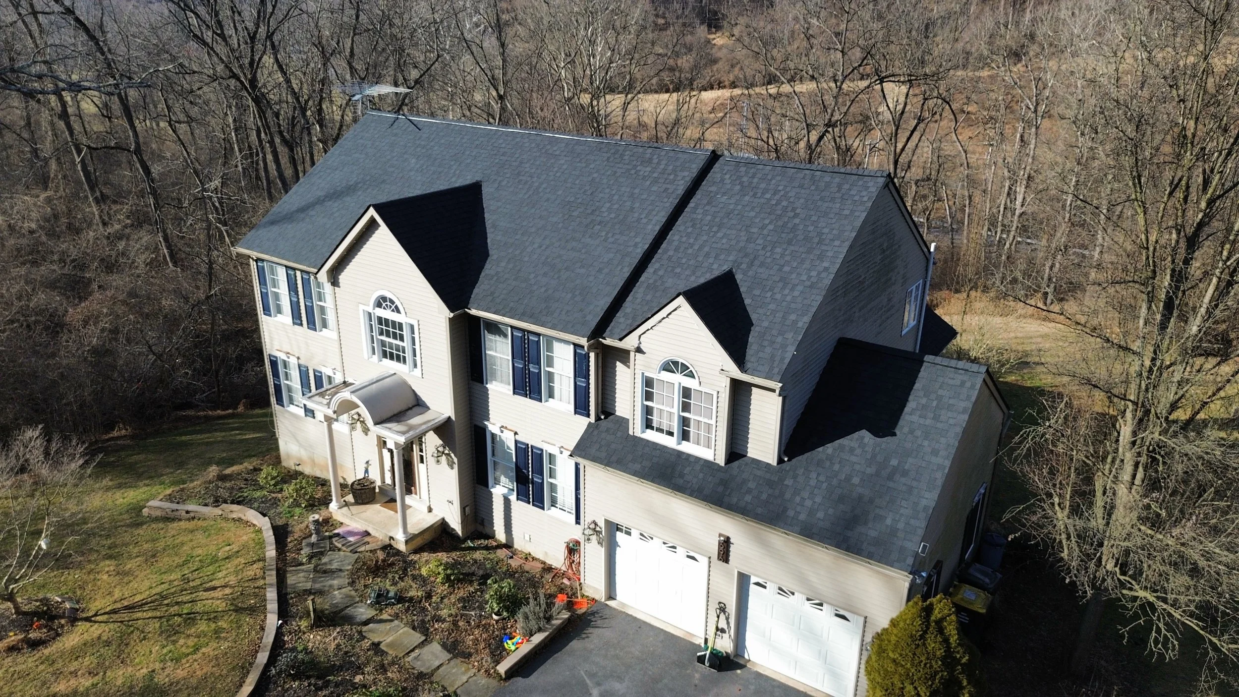 Aerial view of a two-story beige house with a dark gray roof, surrounded by trees and a manicured lawn, with a small front porch and a two-car garage in West Chester, PA.