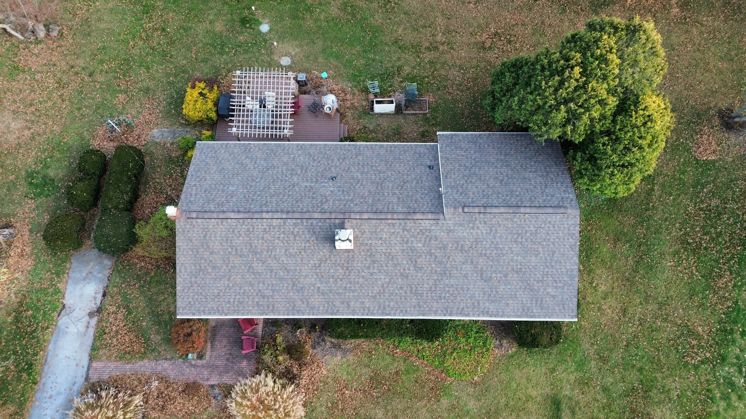 Aerial view of a house with a gray shingle roof, surrounded by trees, bushes, a small wooden deck with patio furniture, and a winding concrete path in the yard in West Chester, PA.