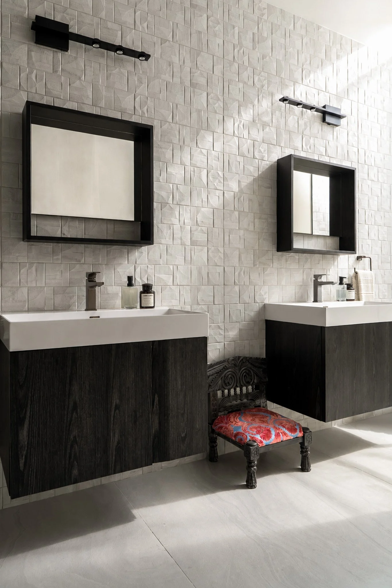 Modern bathroom with black-framed mirrors, white tiled walls, black sinks, and a decorative chair with a red patterned seat.