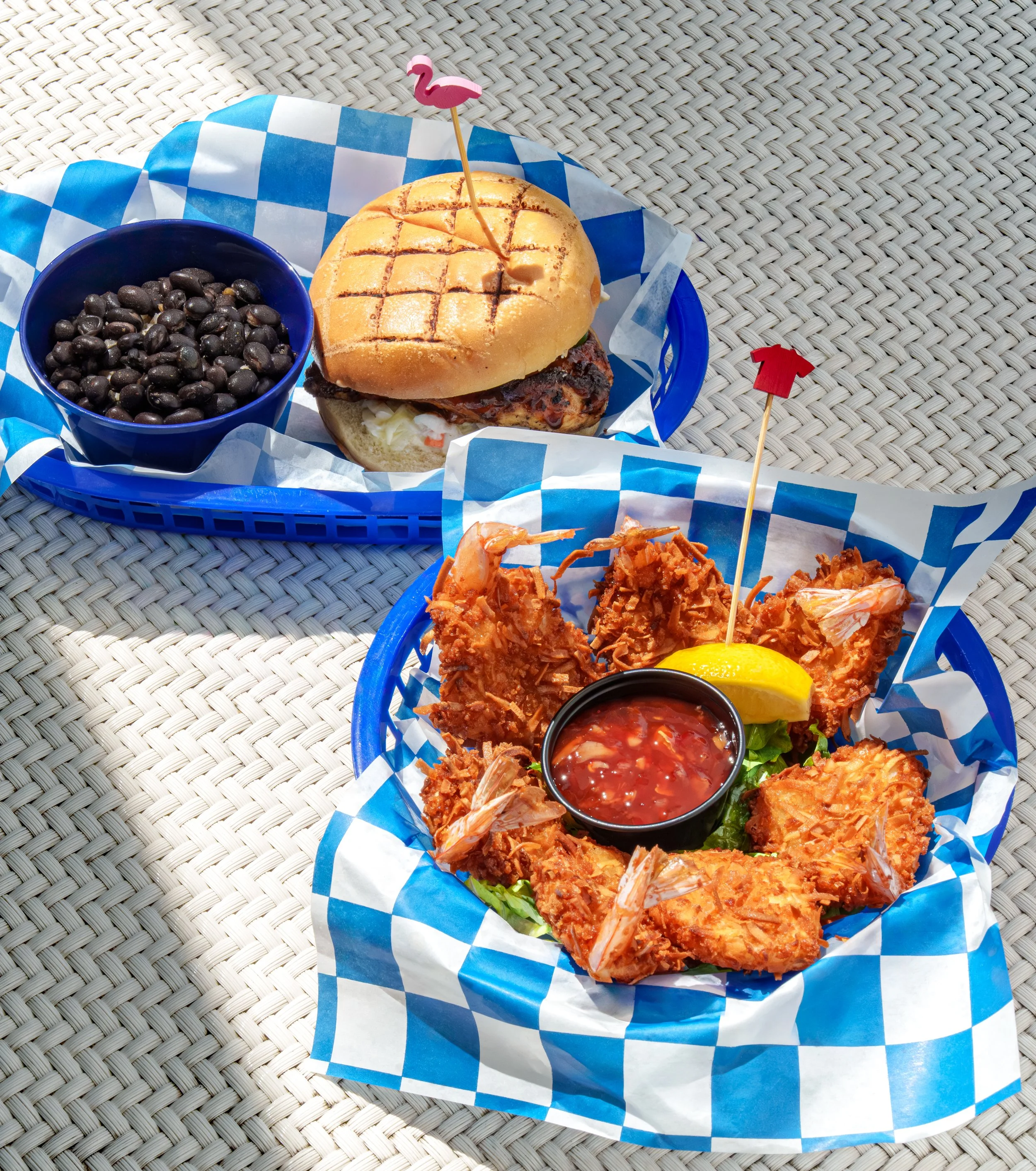 Overhead food photograph of a burger basket and crispy coconut shrimp on woven seating featured in a hotel restaurant OTA listing