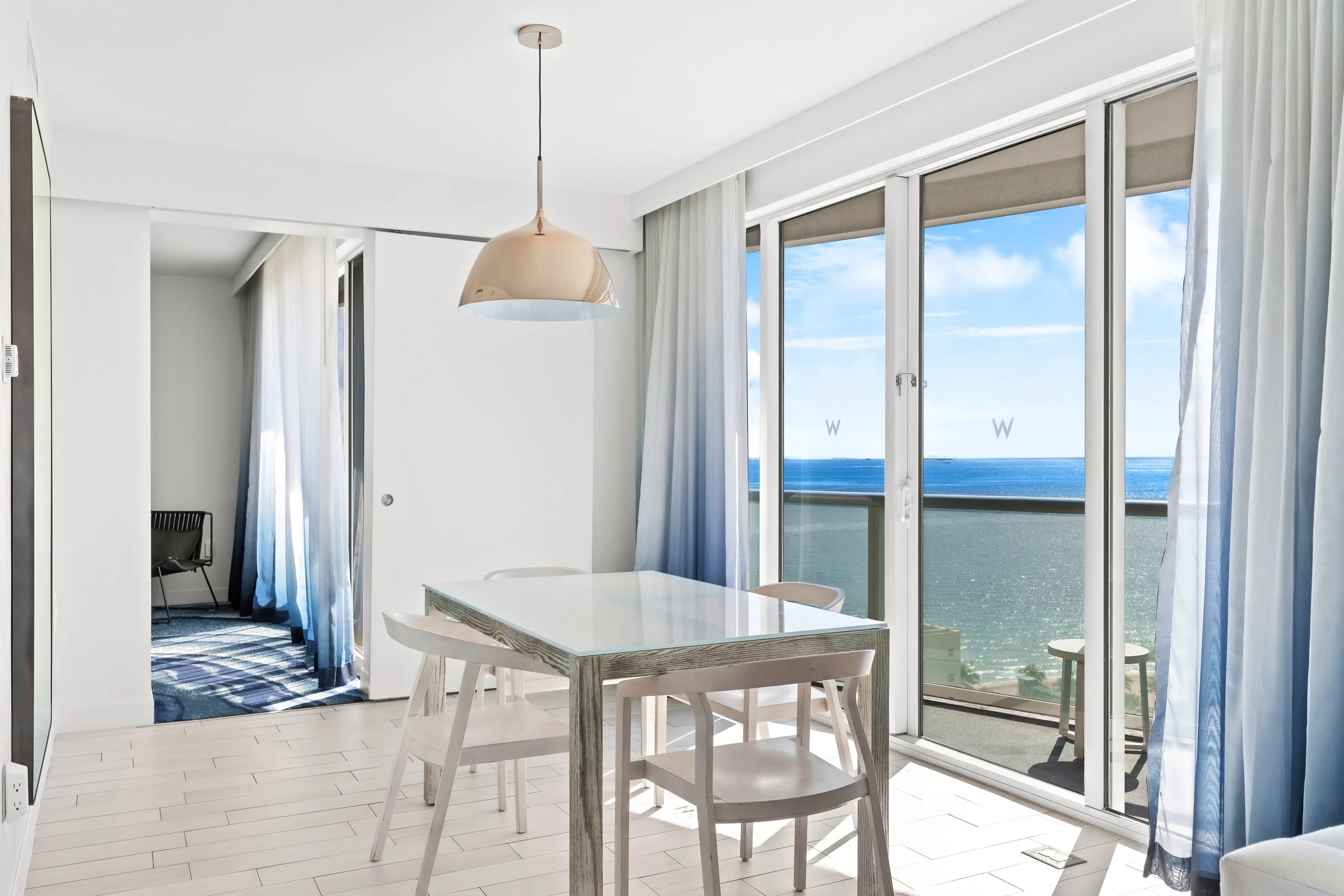 Hotel suite dining area with table and chairs by sliding glass doors and ocean view