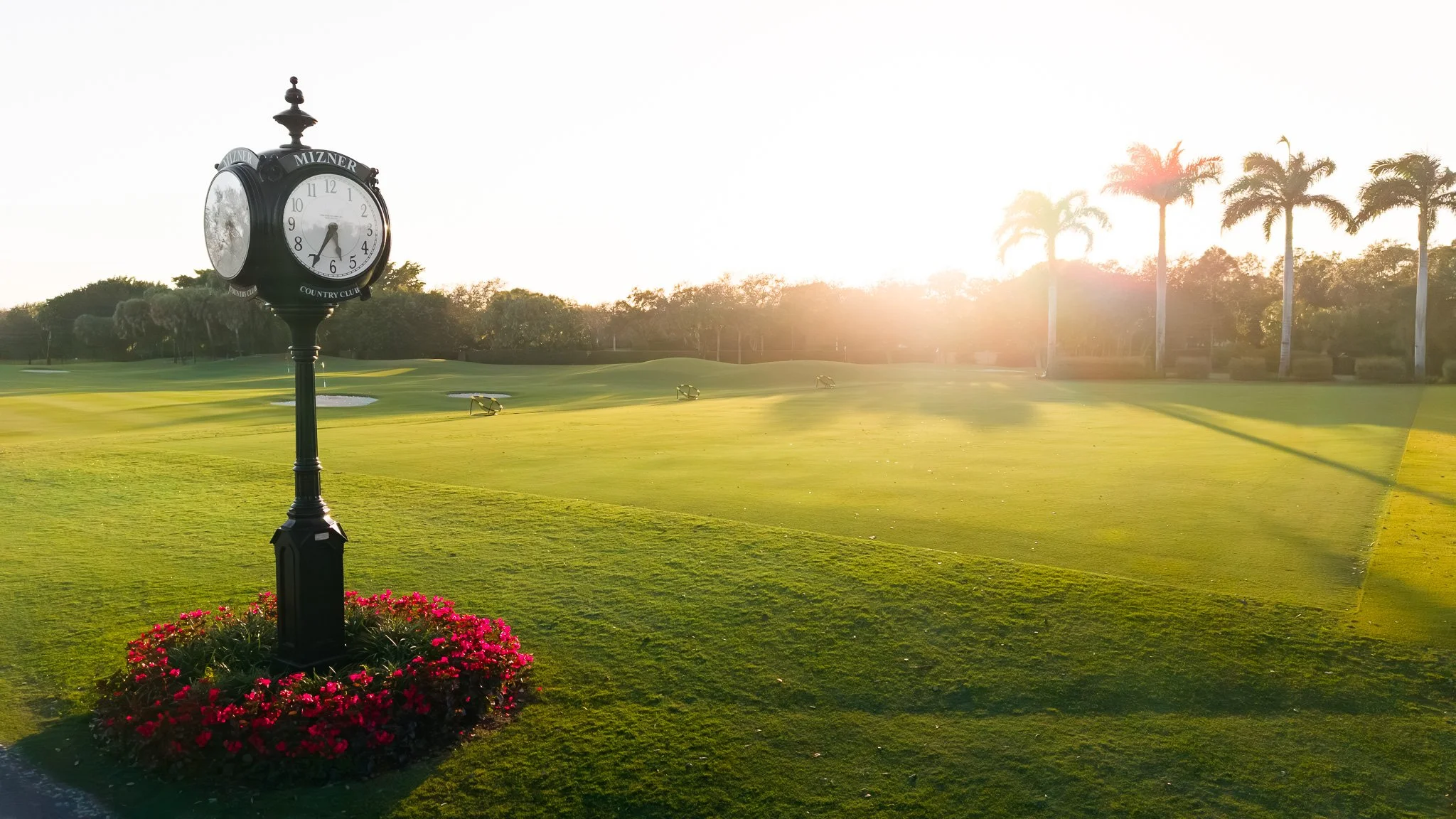 A golf course with a green, sand bunkers, trees, water hazard, and a pathway during sunset.