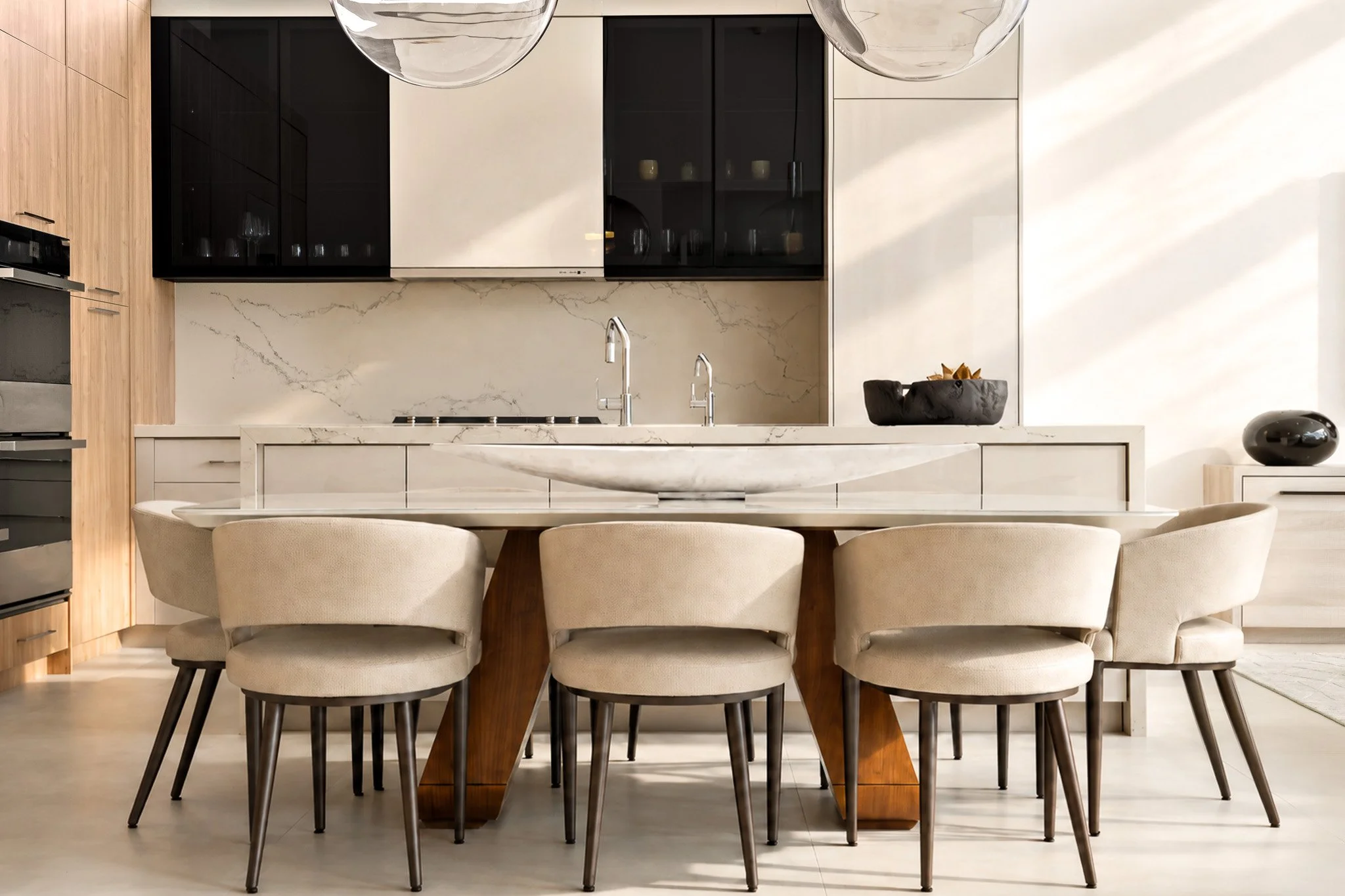 Modern kitchen with a marble island, black and white cabinets, and a dining table with beige upholstered chairs.