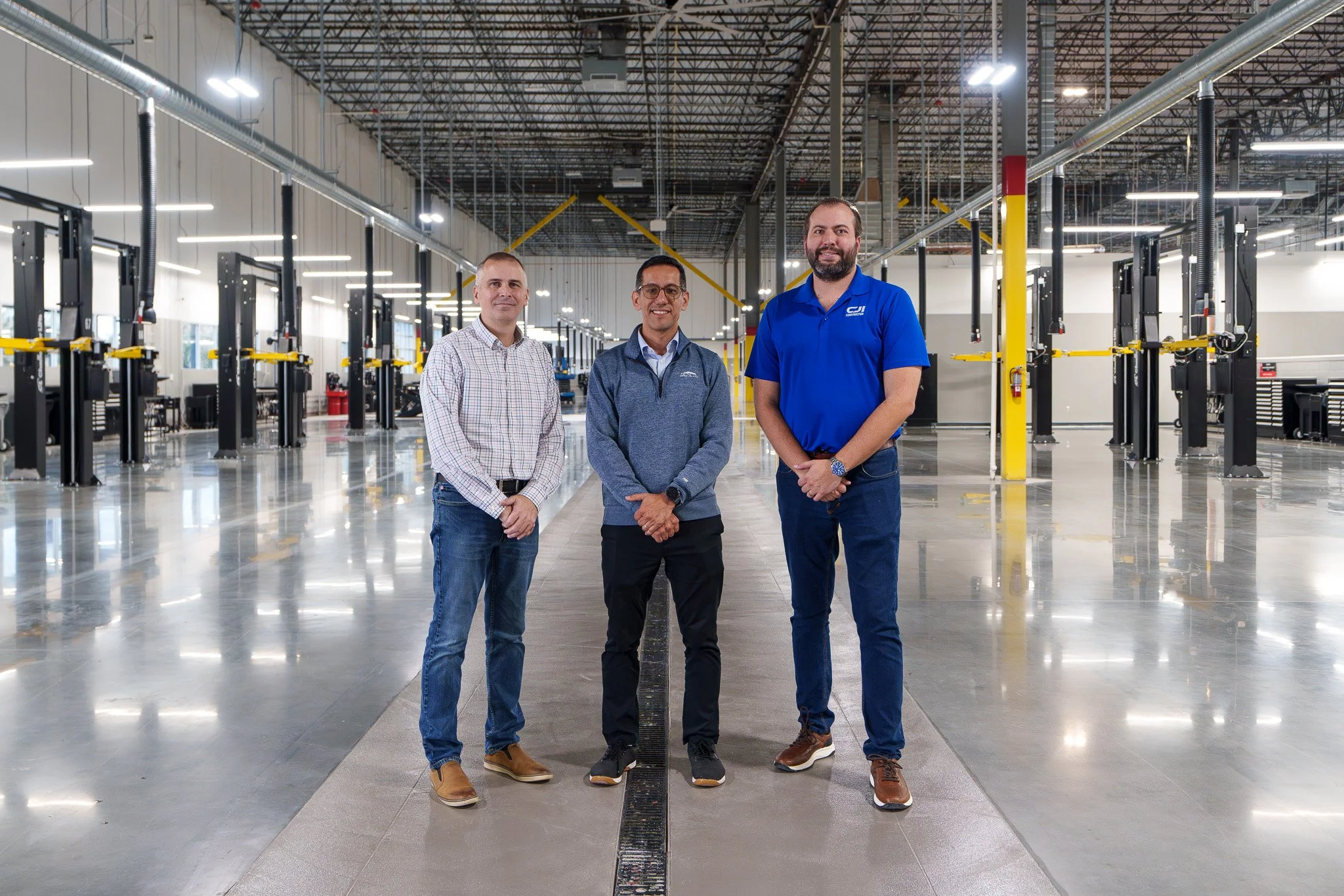 Three men standing inside an industrial or manufacturing facility with machinery and bright lighting.