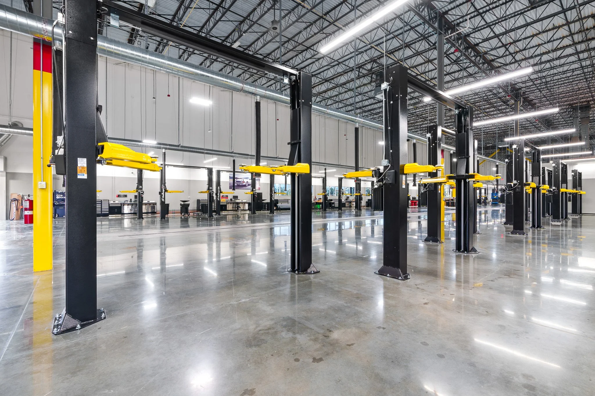 Empty automotive service or repair shop with vehicle lifts, yellow safety locks, polished concrete floors, and high ceiling with exposed metal beams and bright lighting.