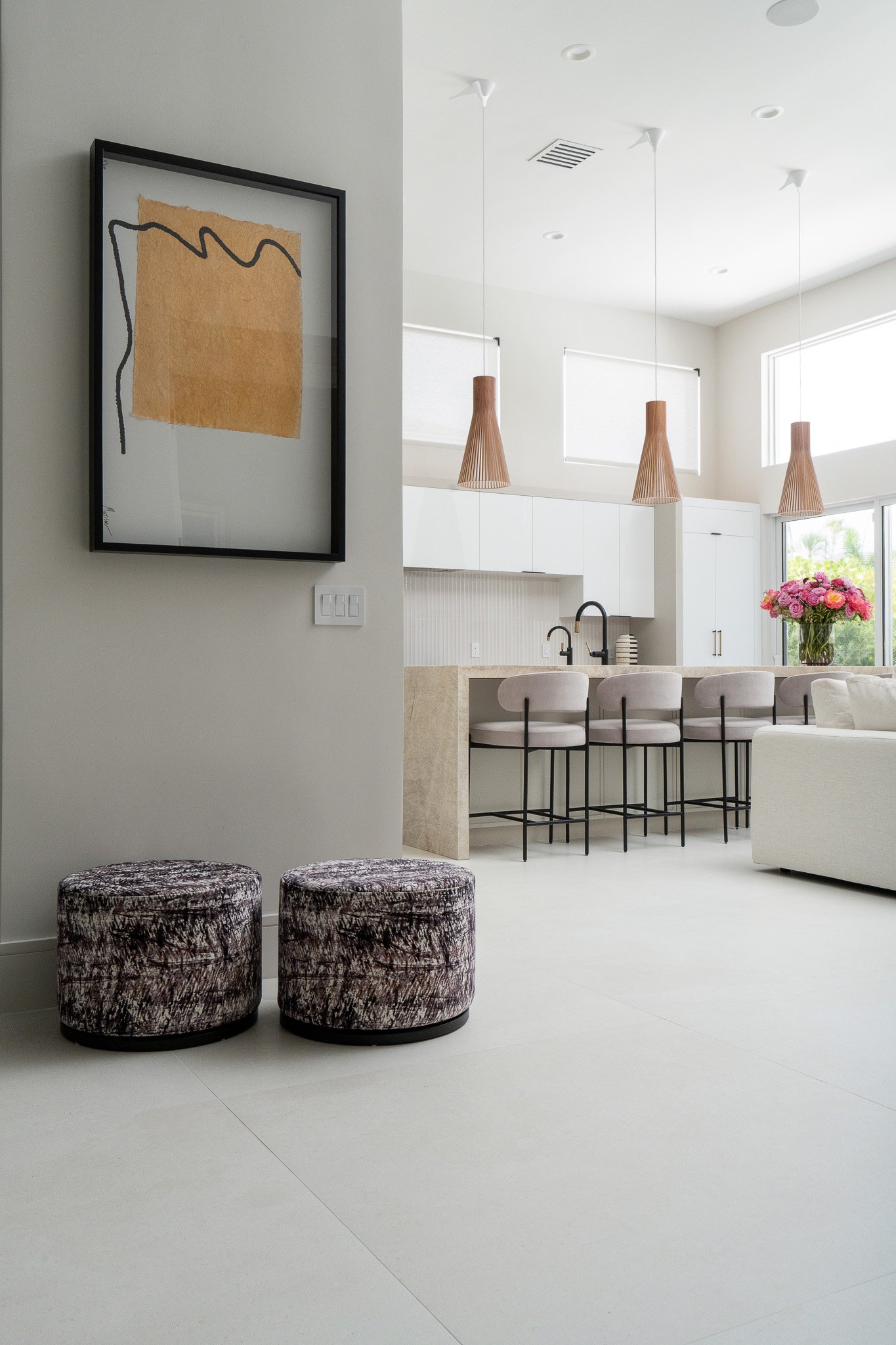 Modern kitchen and living space with pendant lights, bar seating, a vase of pink flowers, and abstract wall art.