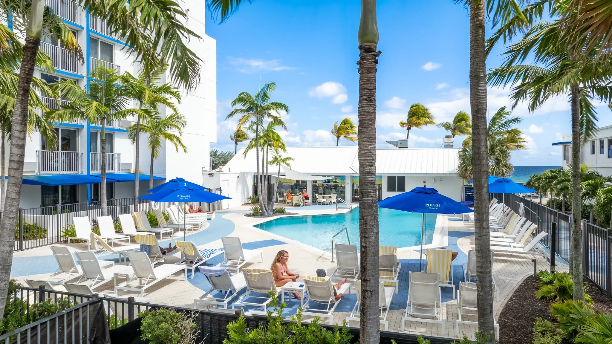 Professional hotel photograph of a Key West boutique resort pool with palm trees, blue umbrellas, and lounge chairs ideal for OTA listing hero images