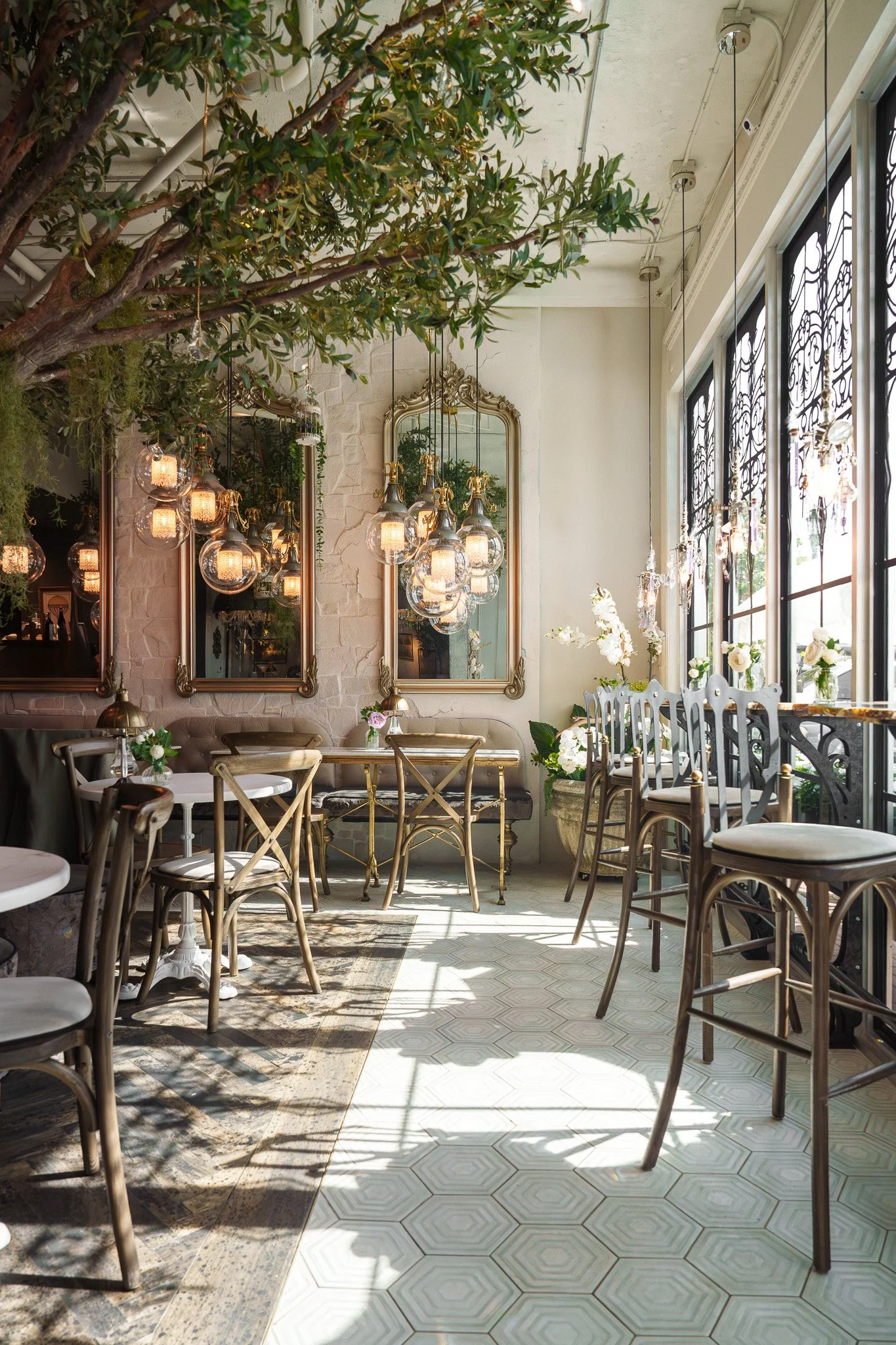 Sunlit restaurant interior with hanging glass globe pendant lighting, vintage mirrors, and lush greenery prepared for a hospitality photo shoot