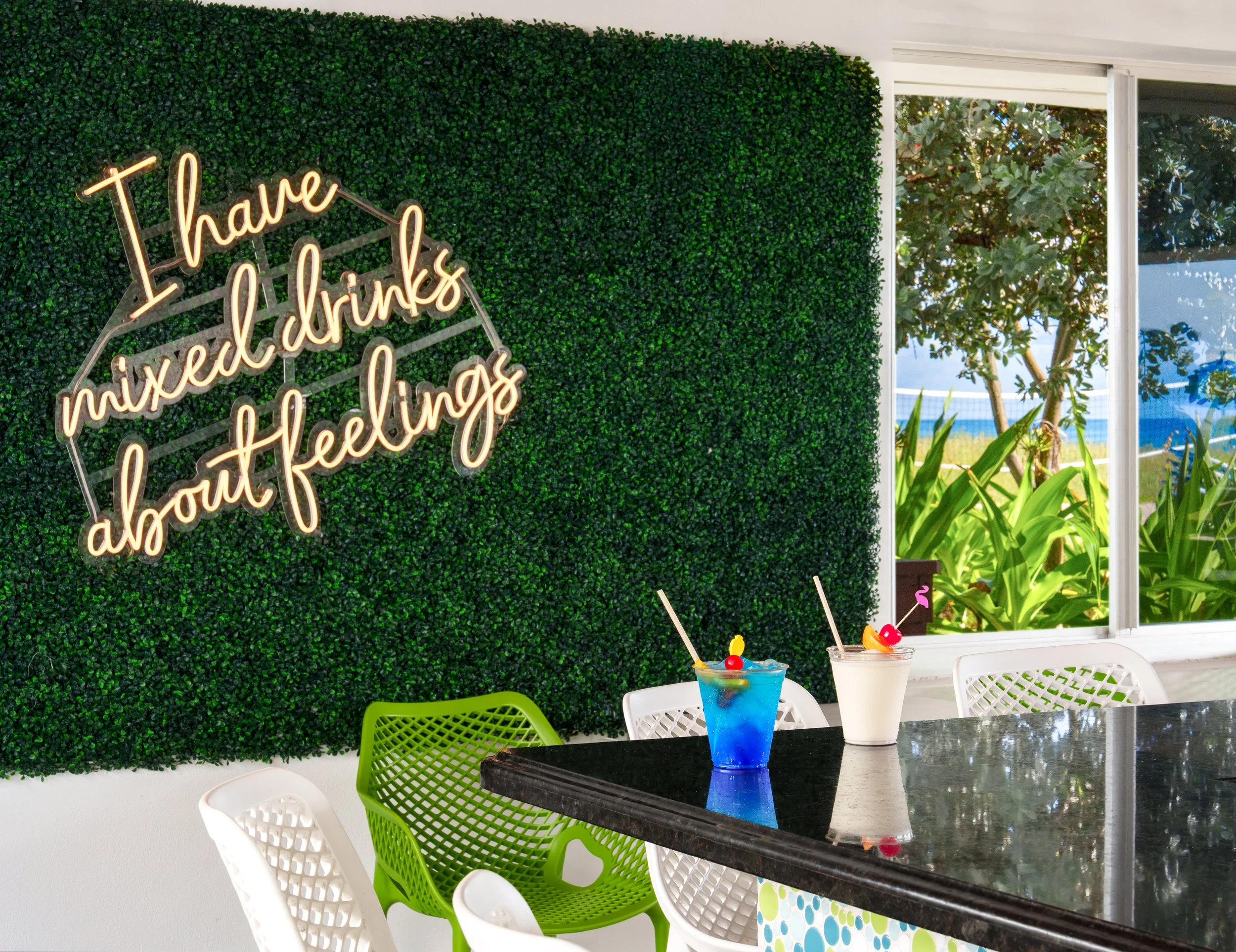 Hotel bar amenity photograph featuring an "I have mixed drinks about feelings" neon sign and tropical cocktails for an OTA hotel listing