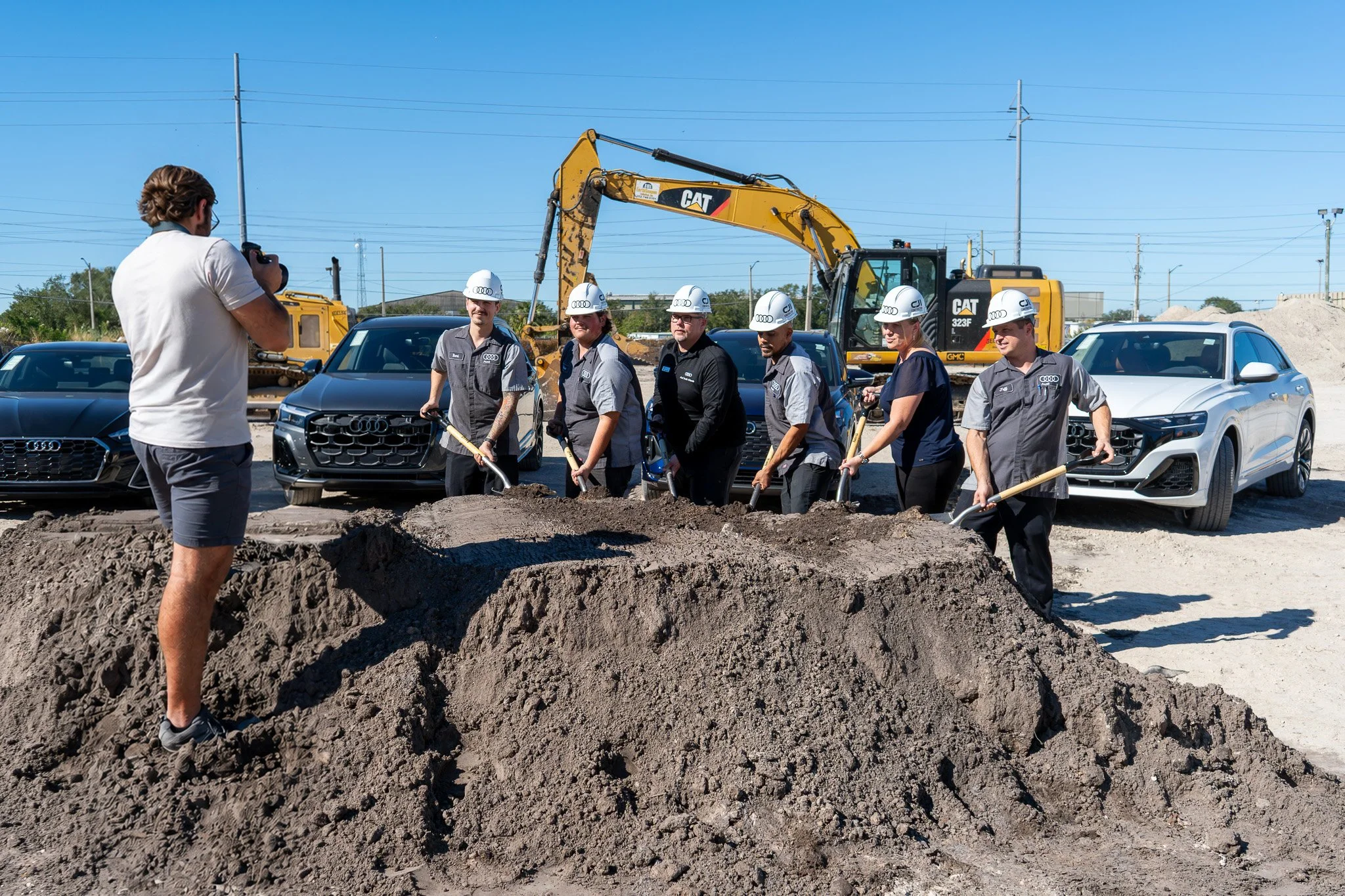 Commercial construction groundbreaking ceremony with executives holding shovels and an excavator in the background at a South Florida development site