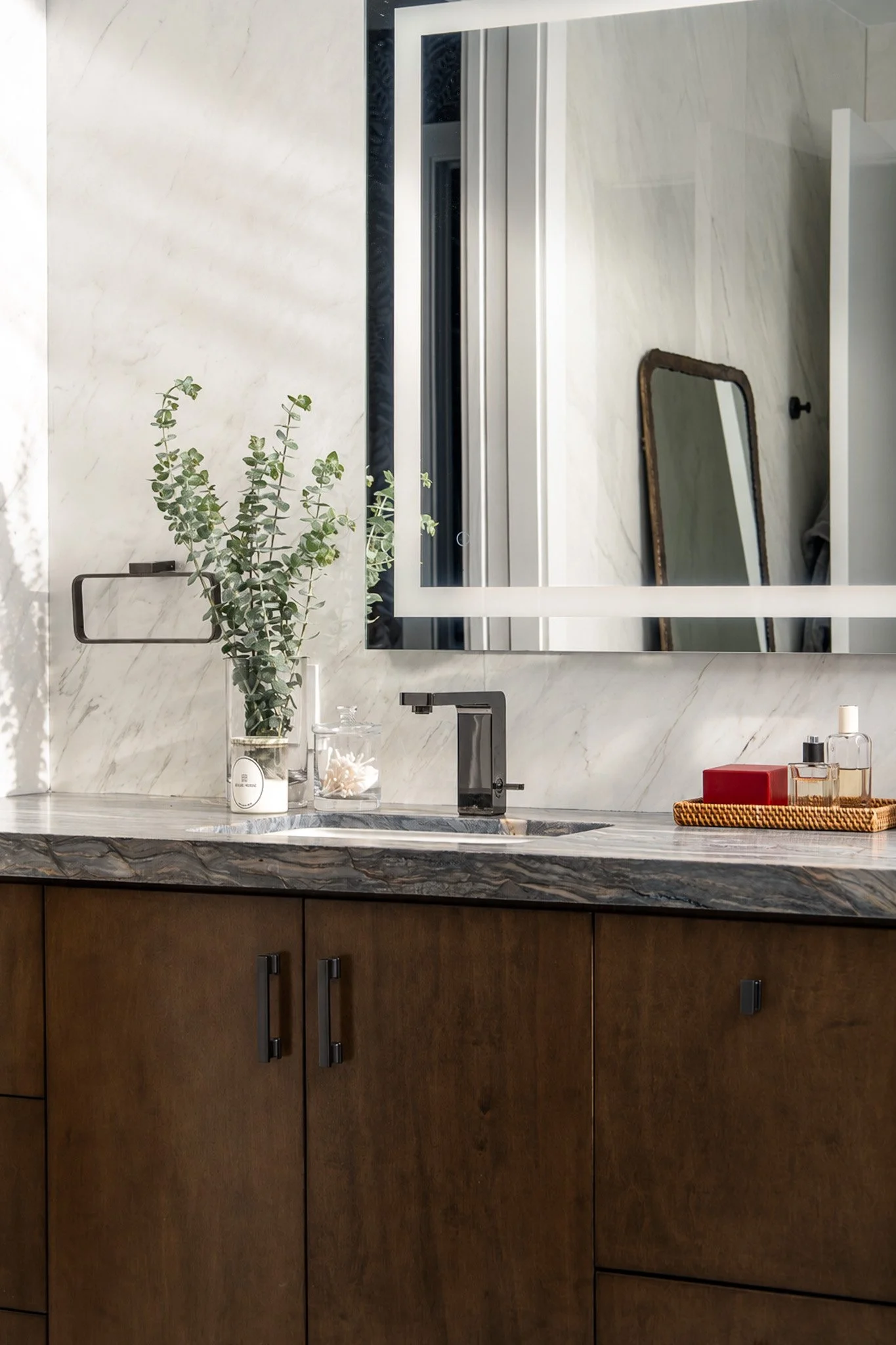 A bathroom vanity with a marble countertop, a potted plant, a mirror, and cabinet drawers with black handles.