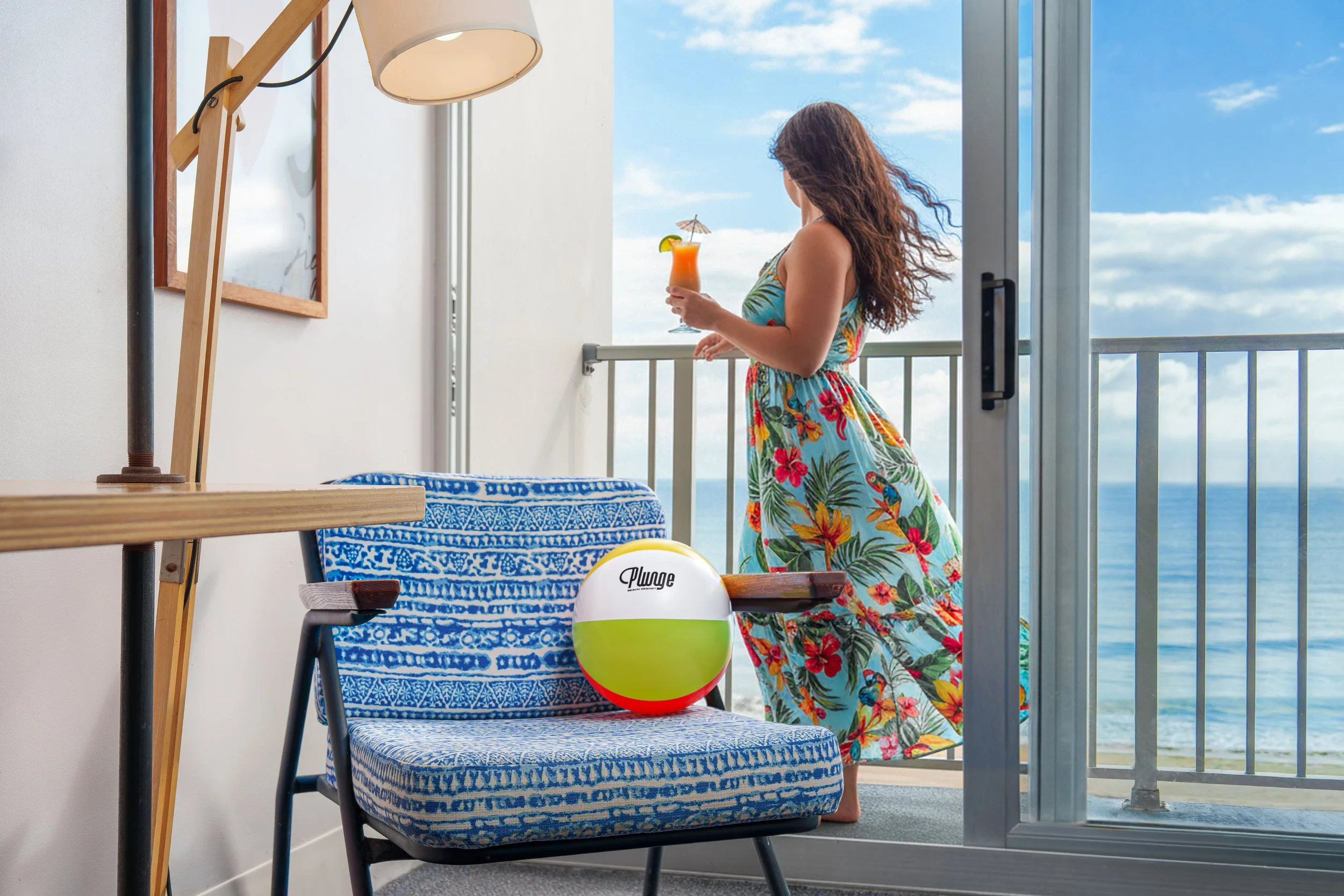Lifestyle hotel photograph of a guest in a floral dress holding a cocktail on a private oceanview balcony at a South Florida resort