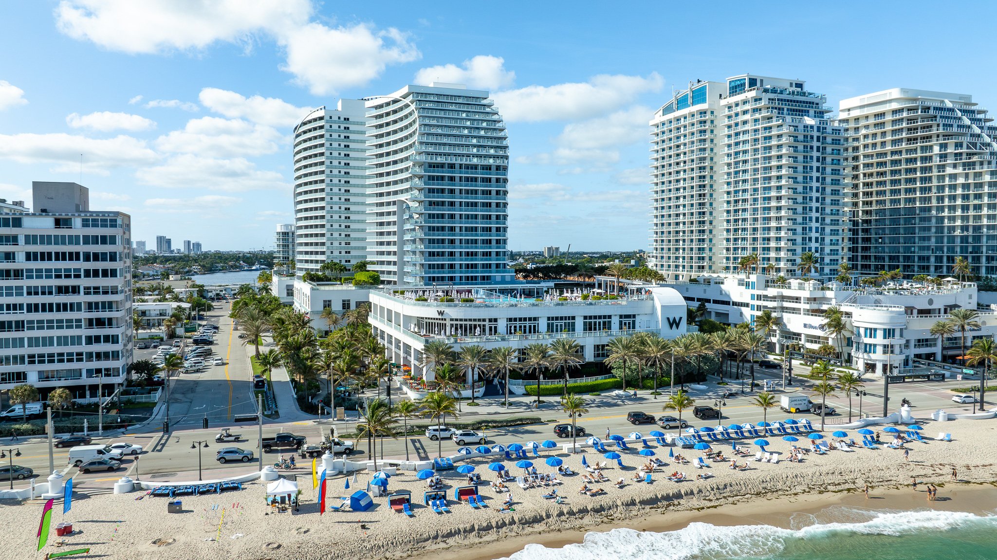 Aerial view of beachfront hotels with cabanas, umbrellas, and crashing waves on the South Florida coast