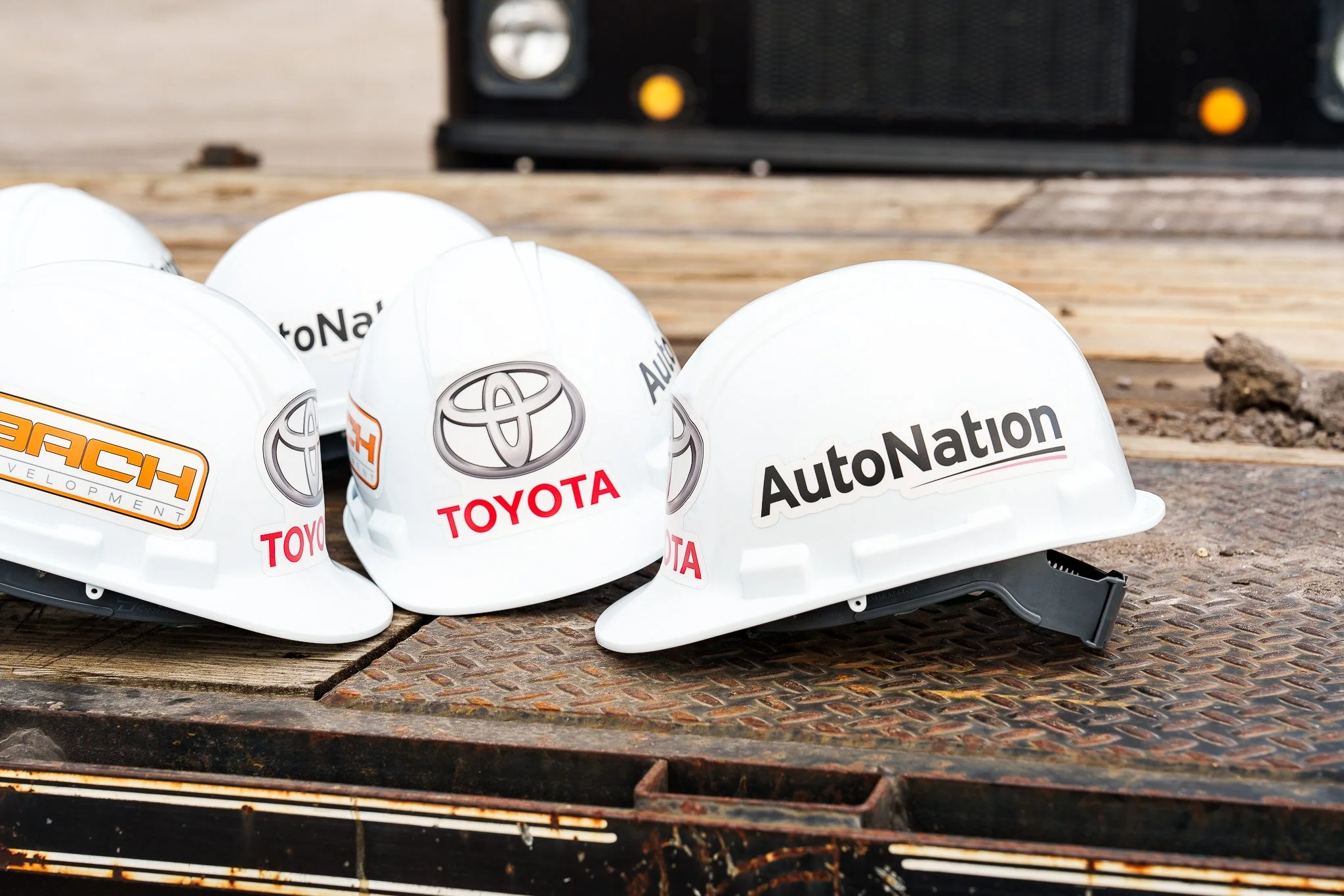 Several white safety helmets with logos and text, placed on a rusty surface outdoors, with a blurred background.
