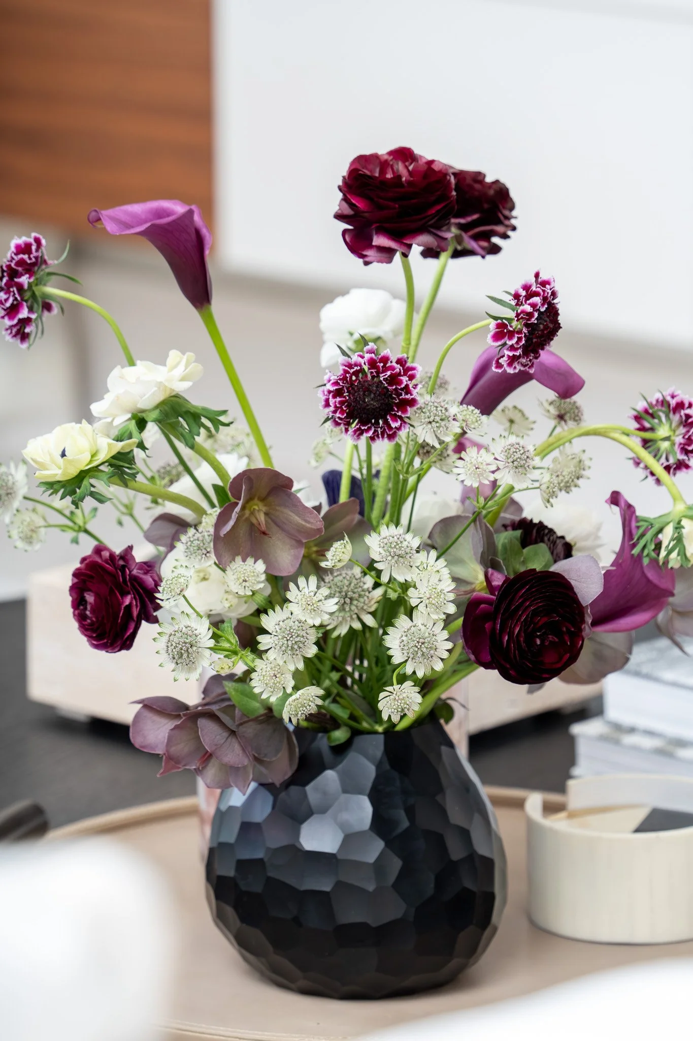 A bouquet of dark purple, white, and pink flowers in a black geometric vase.