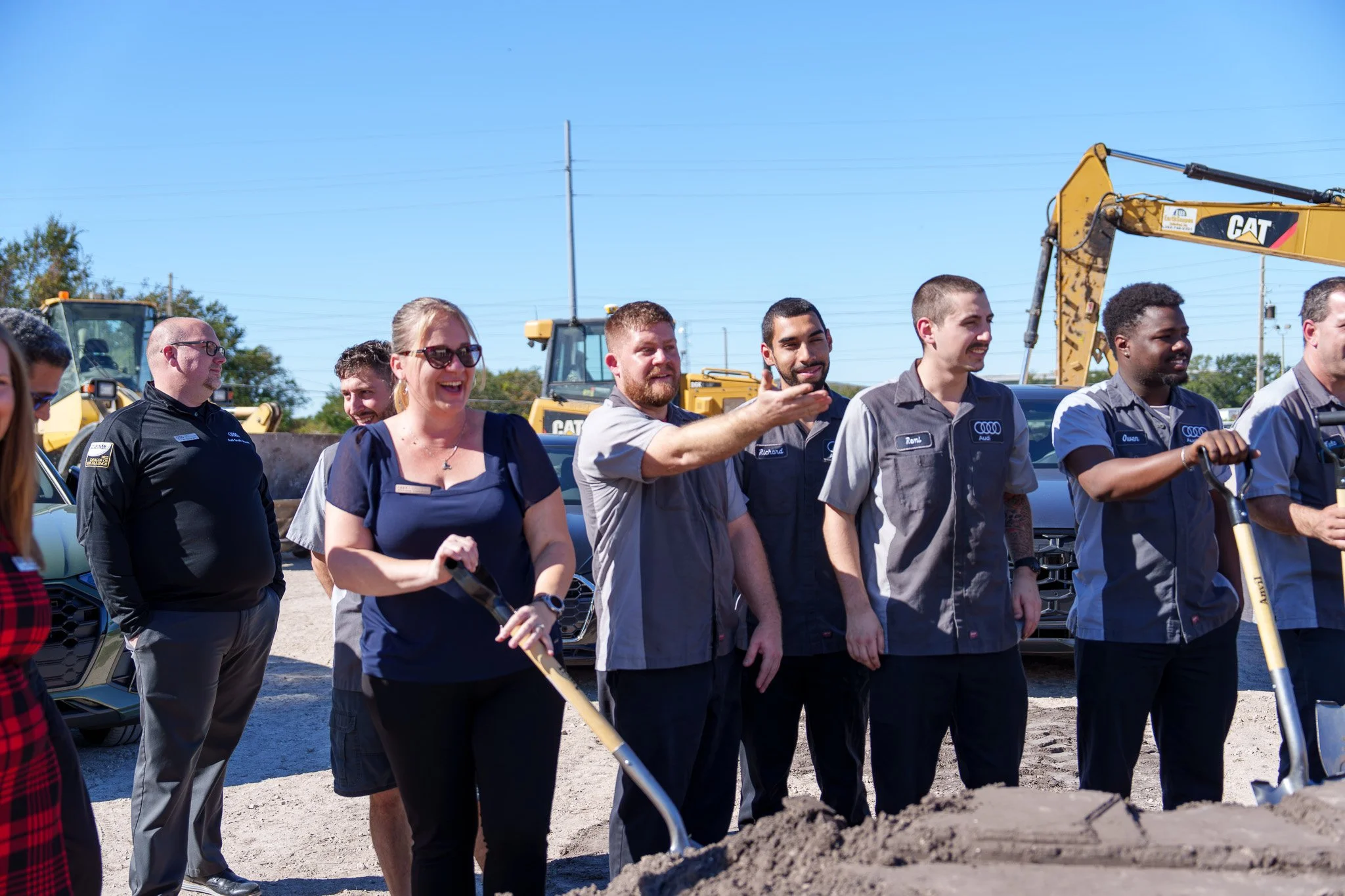 Group of people standing outdoors, with construction equipment and blue sky in background.